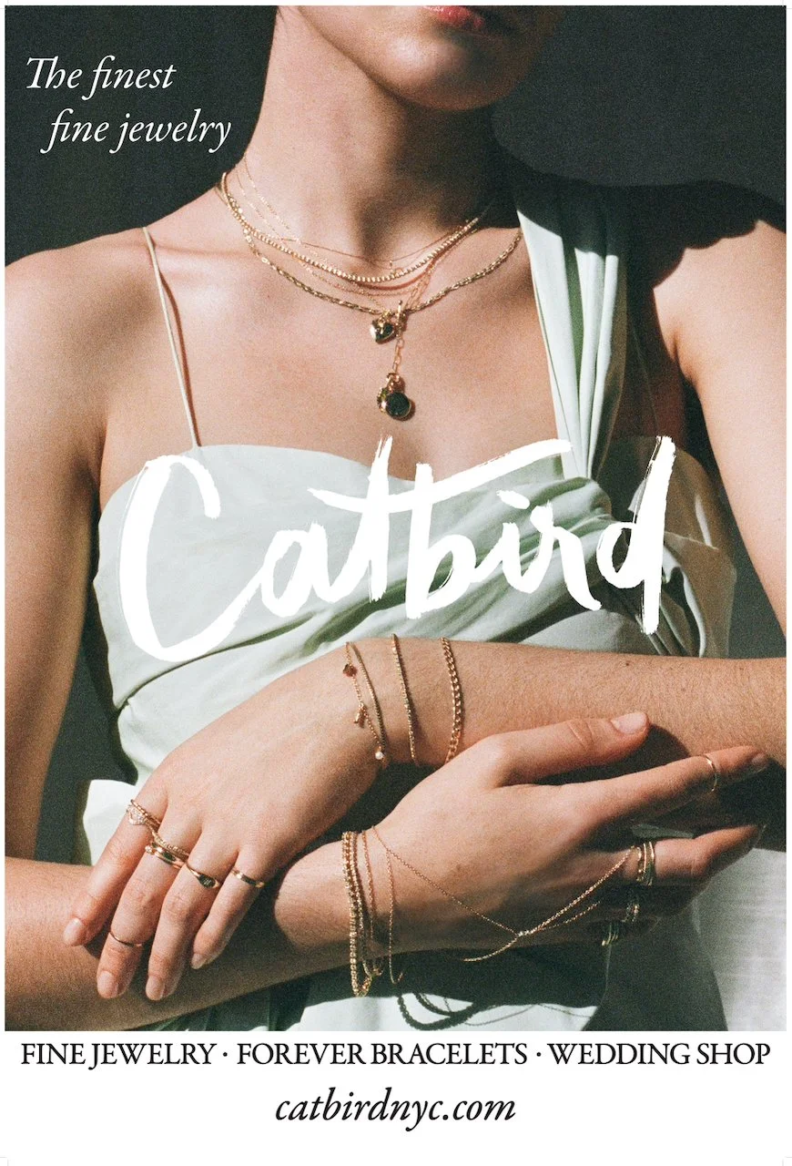 A woman wearing layered gold necklaces and multiple delicate gold rings and bracelets, with the text "The finest fine jewelry" and "catbird" in large white script, promoting a jewelry shop.