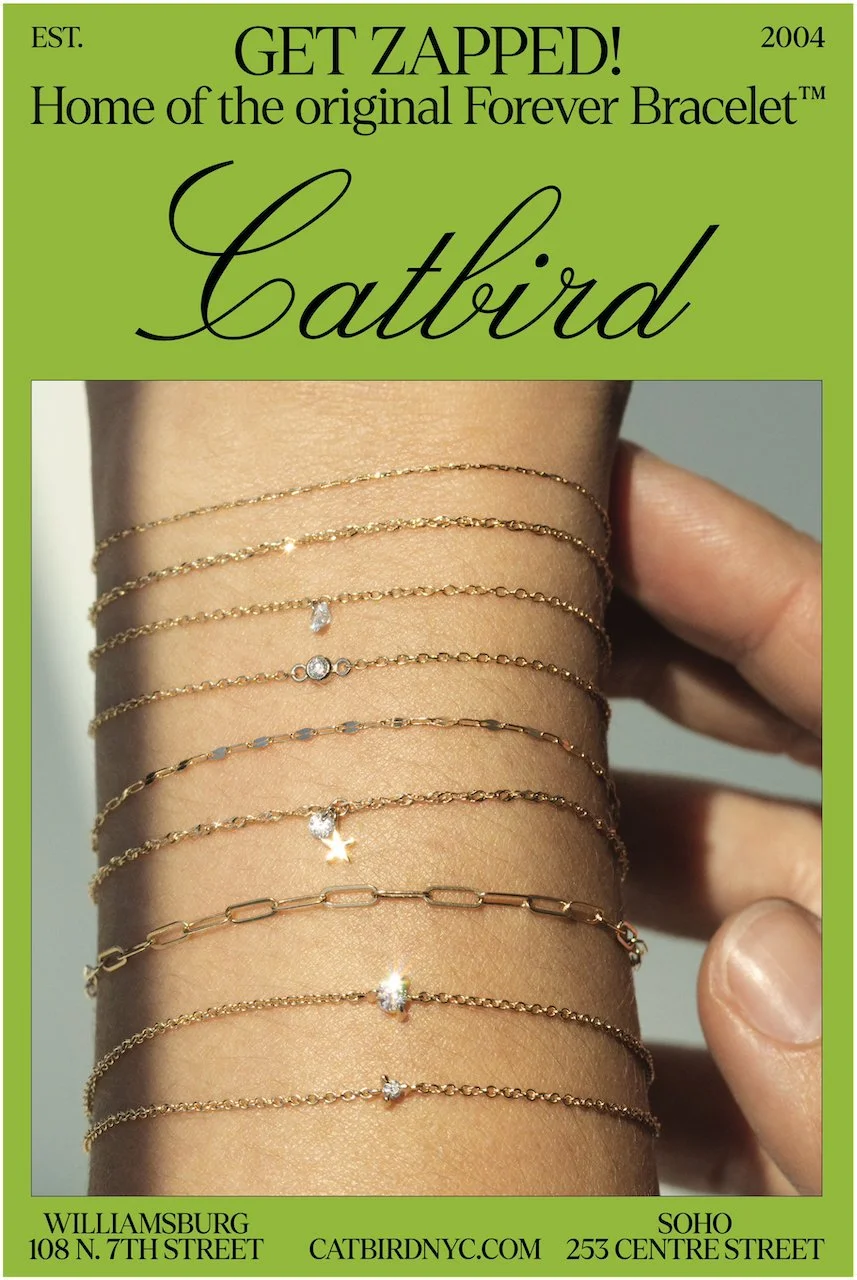 A close-up of a person's wrist showing multiple gold necklaces with various delicate chain designs and small pendants, set against a light gray background, with a green border featuring text about Catbird jewelry store in Williamsburg and Soho.