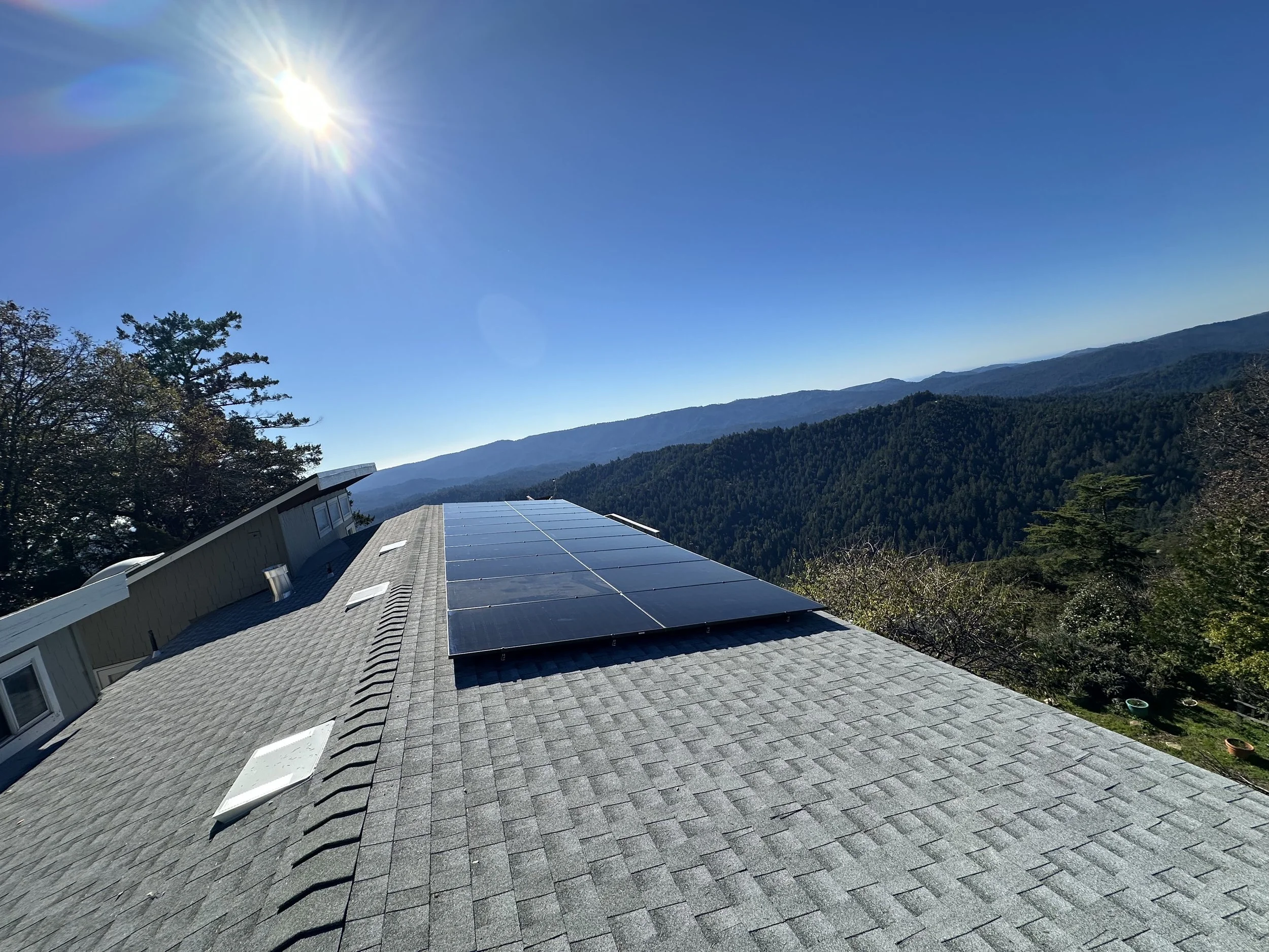 Solar panels installed on the roof of a house in a mountainous area with a clear blue sky and the sun shining brightly.