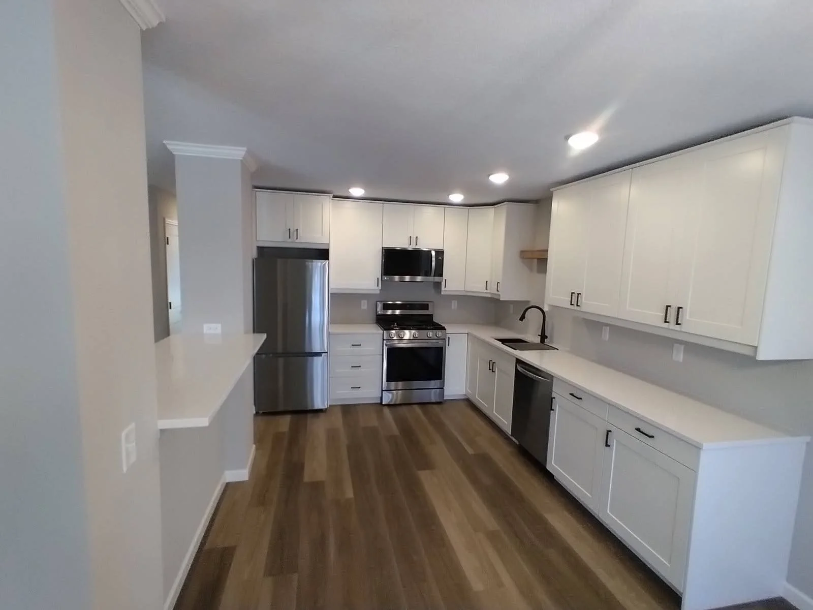 Modern kitchen with white cabinets, stainless steel refrigerator, oven, microwave, and dishwasher, black faucet, and wooden flooring.