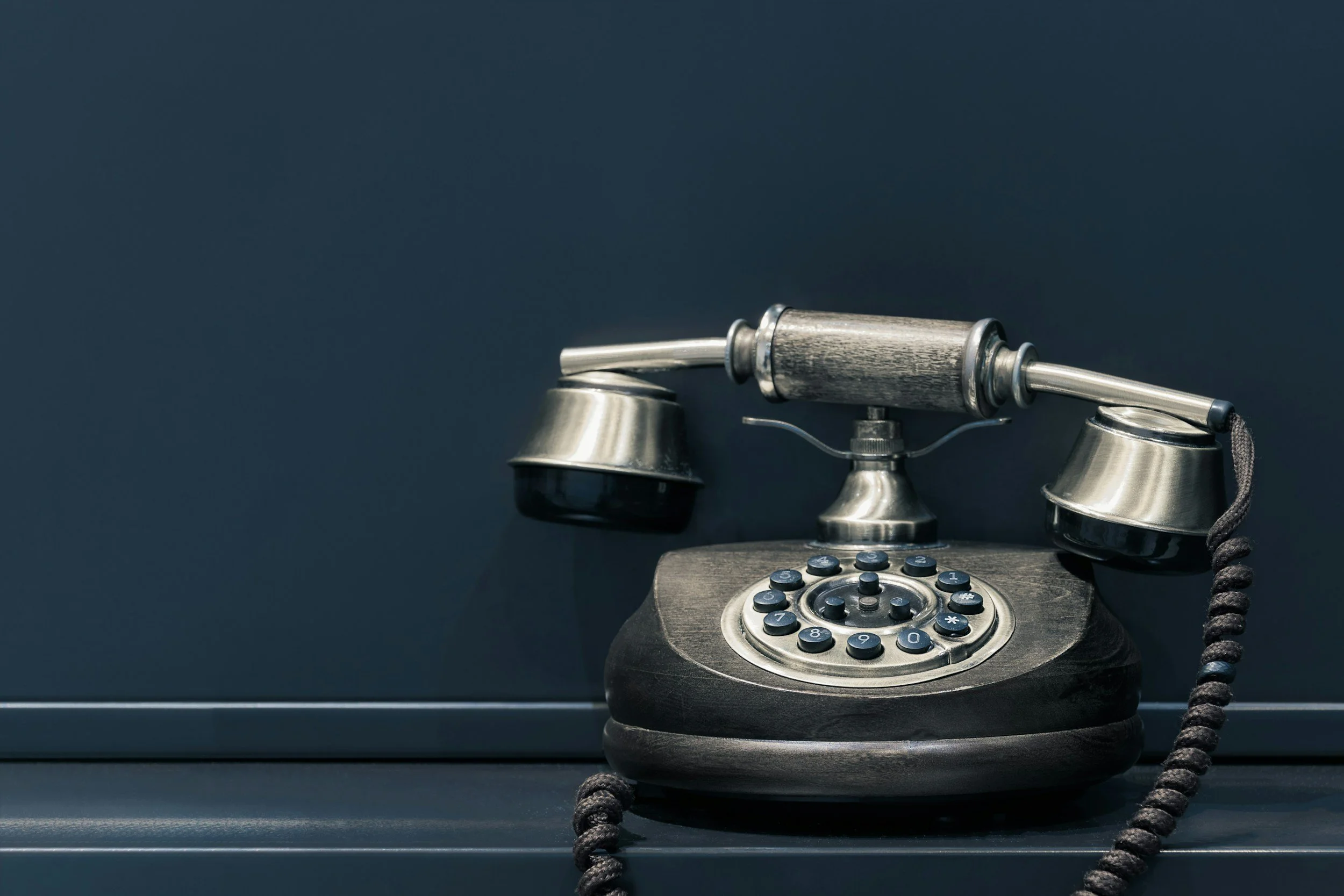 Vintage rotary telephone with a black base and metallic accents, placed on a dark surface against a dark background.