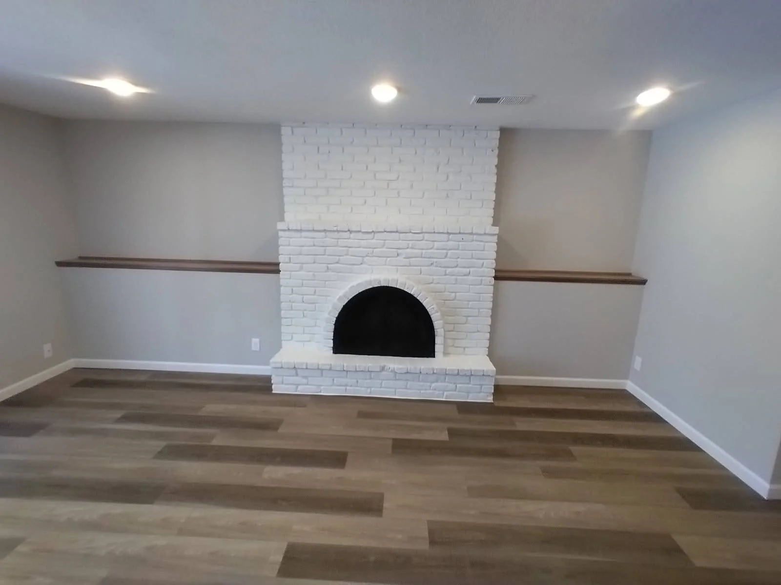 Living room with a white brick fireplace, light gray walls, wooden flooring, and recessed ceiling lights.