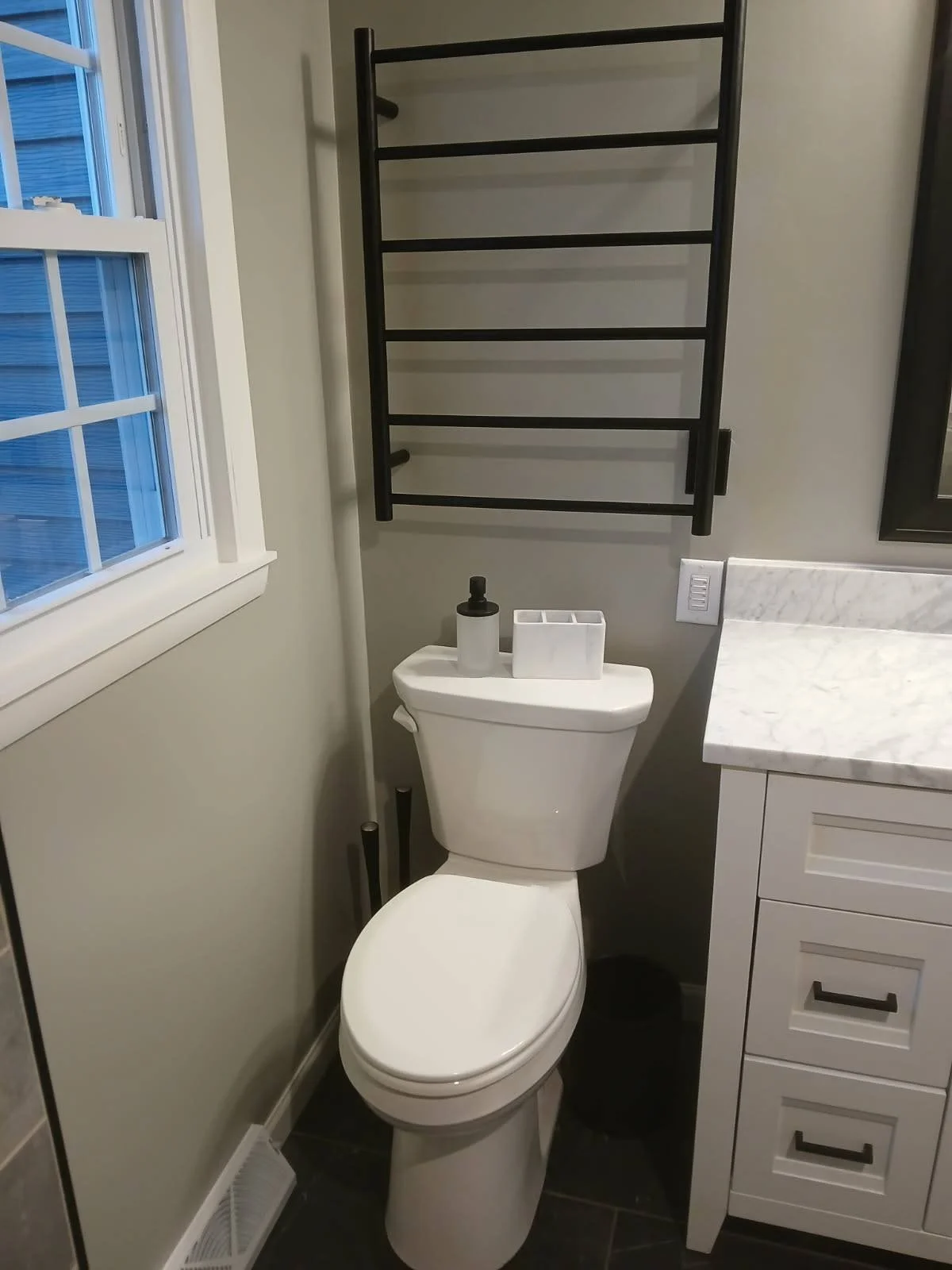 Bathroom with a toilet, black towel rack, countertop, and window.