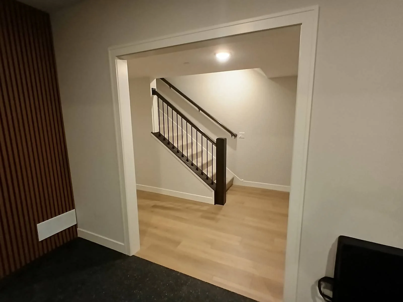 View of a staircase with a wooden and black metal railing in an indoor residential space, with beige walls and hardwood flooring.