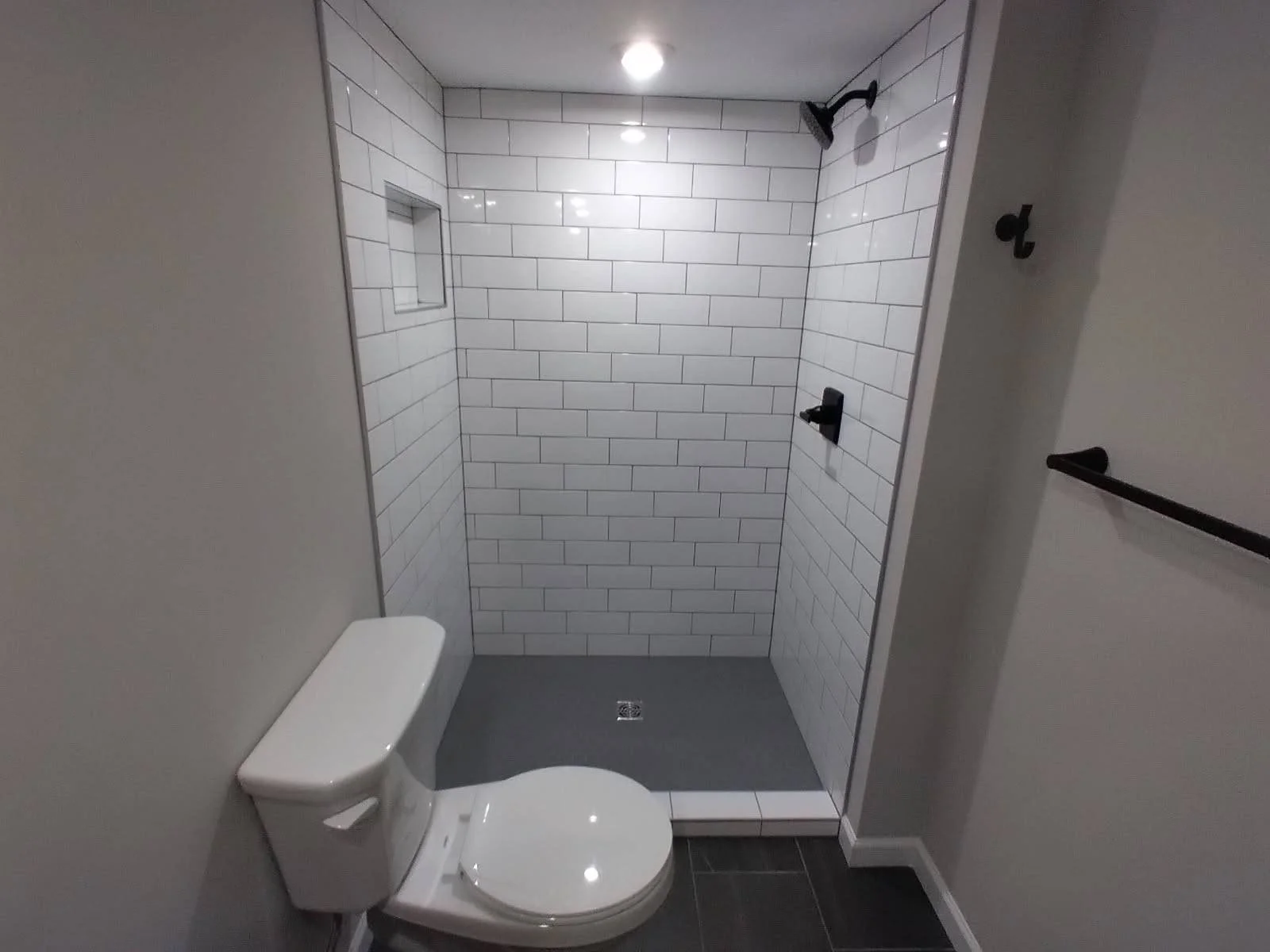 Bathroom with a toilet and a walk-in shower with white subway tile walls and black fixtures.