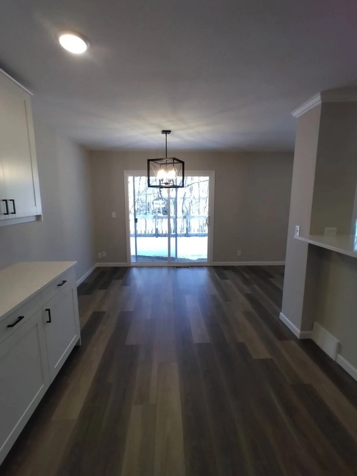 Empty living or dining area with hardwood floors, a sliding glass door leading outside, modern light fixture, and neutral-colored walls.