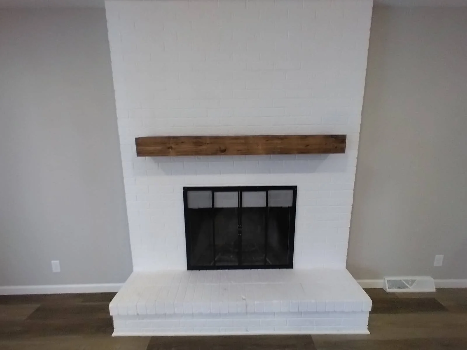White brick fireplace with a black metal frame and glass doors, a wooden mantel, and a brick hearth.