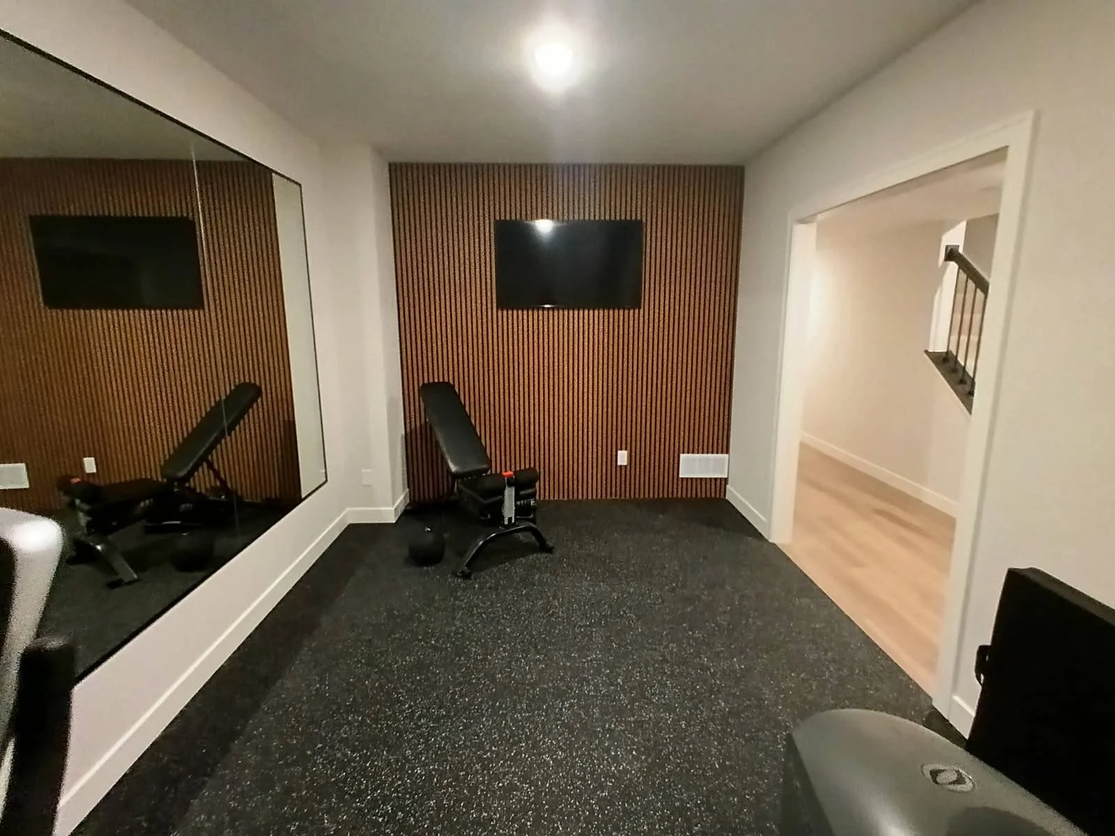 Home gym with a black workout bench, vinyl weight, and a large mirror on the wall reflecting the room.