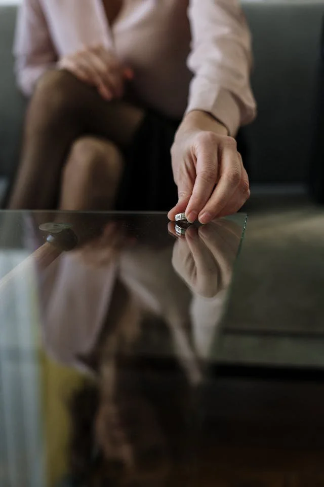 A person placing a coin on a glass surface, with their face and upper body partially visible, sitting on a sofa.
