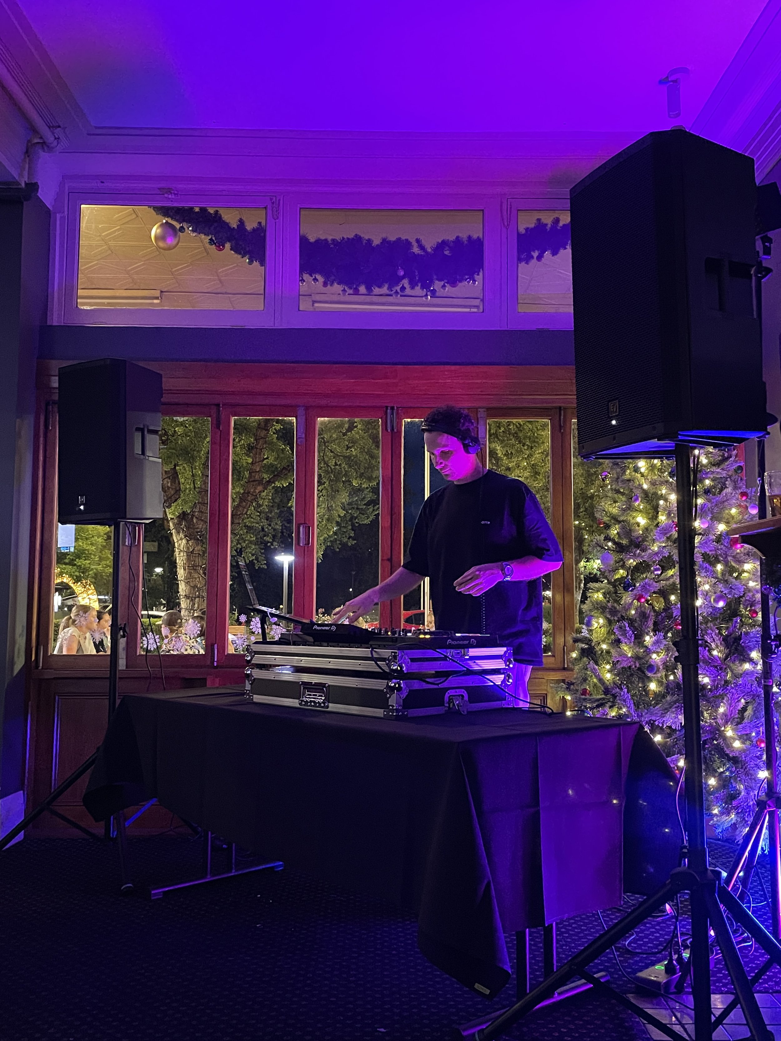 A DJ performs at a Christmas-themed indoor party with a decorated Christmas tree and festive garlands