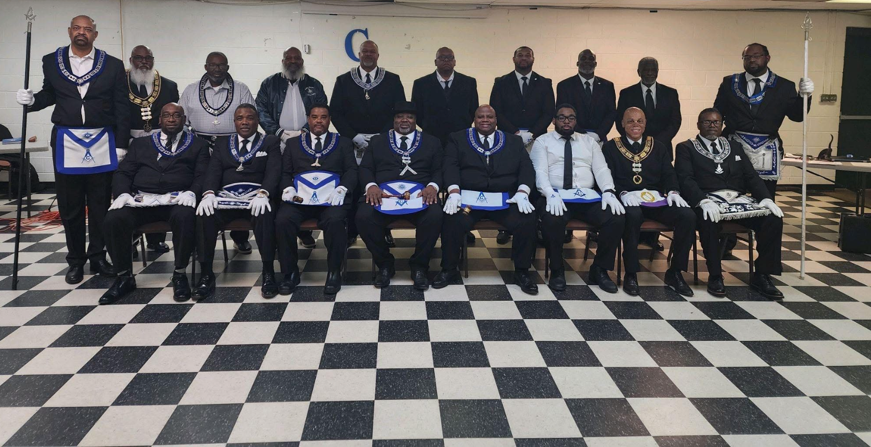 Group of men dressed in formal attire with Masonic regalia, posing for a photo in a room with a checkered black and white floor.