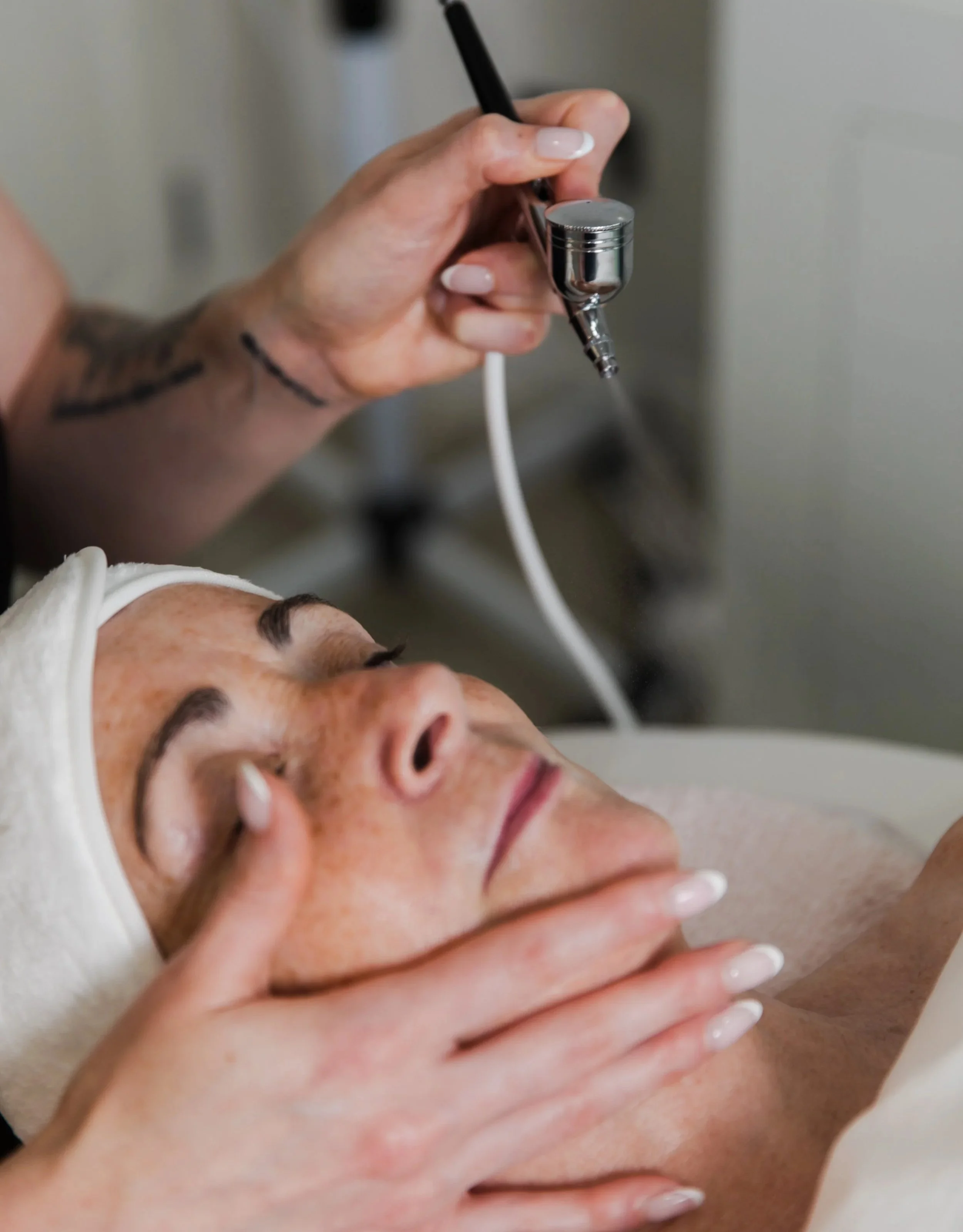 A woman receiving a facial treatment with a steam or extraction device in a spa or clinic setting.