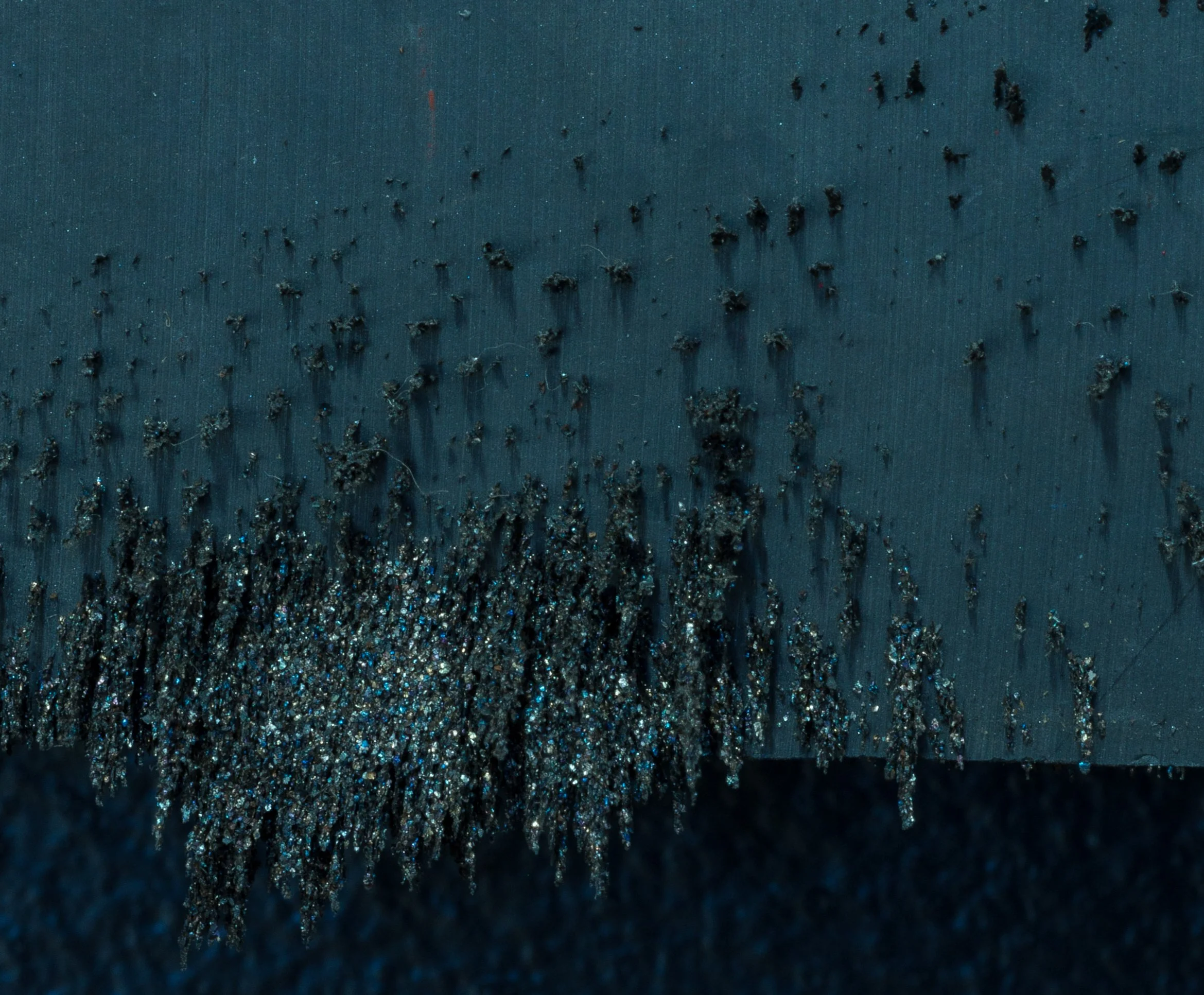 Close-up view of a craft knife with a blade covered in glitter. Glitter is scattered on the cutting surface around the knife.