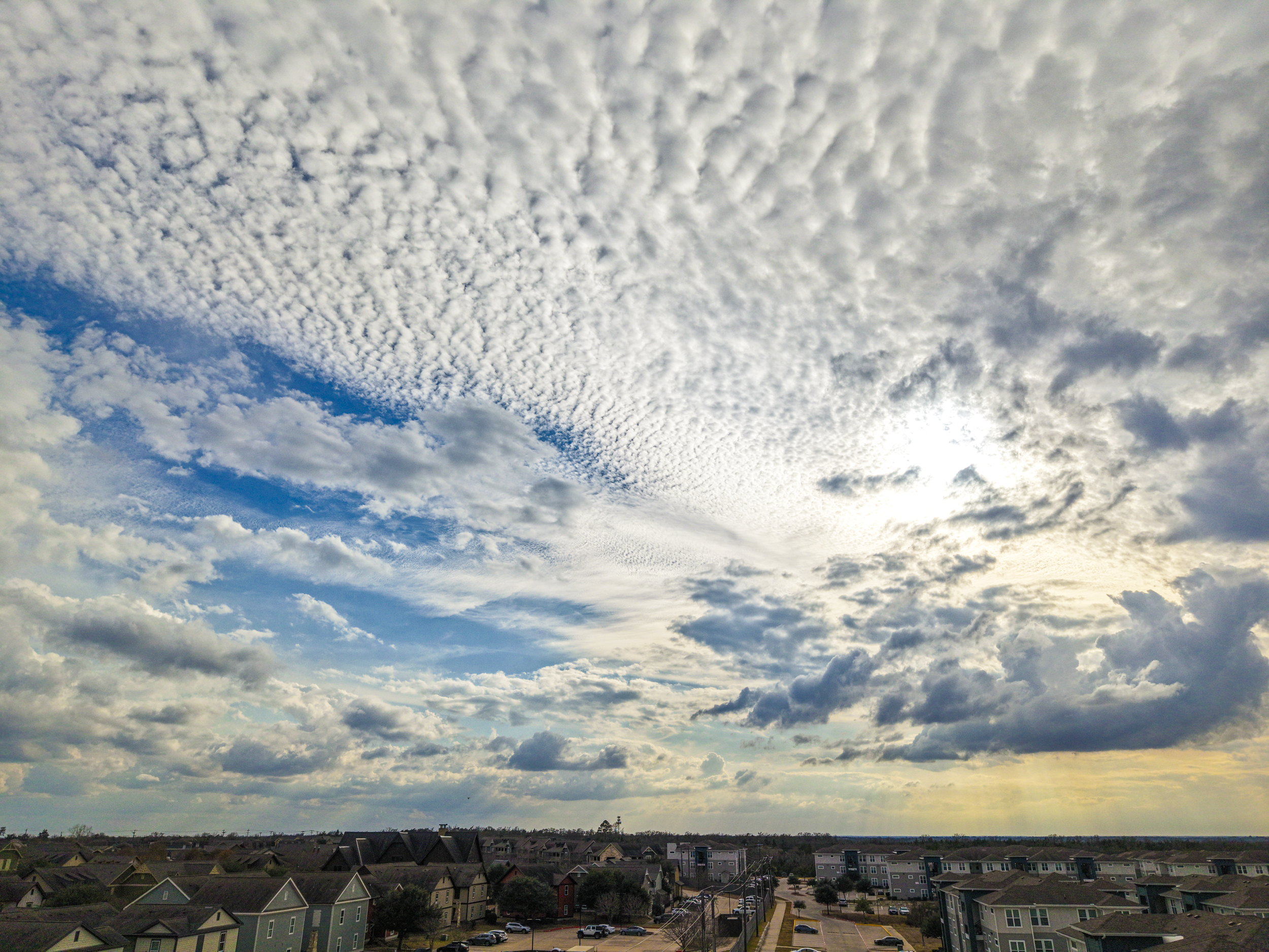 A wide view of a partly cloudy sky over a residential neighborhood with houses and apartment buildings in College Station, Texas.
