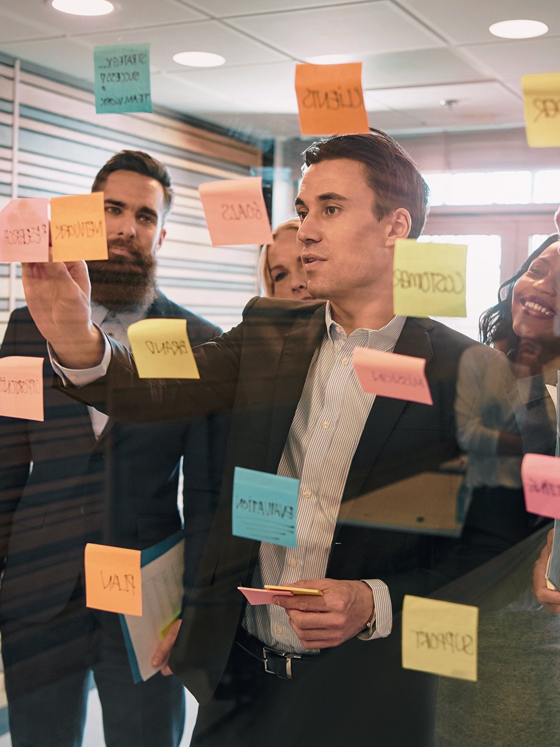 Business team discussing and brainstorming using sticky notes on a glass wall in an office.