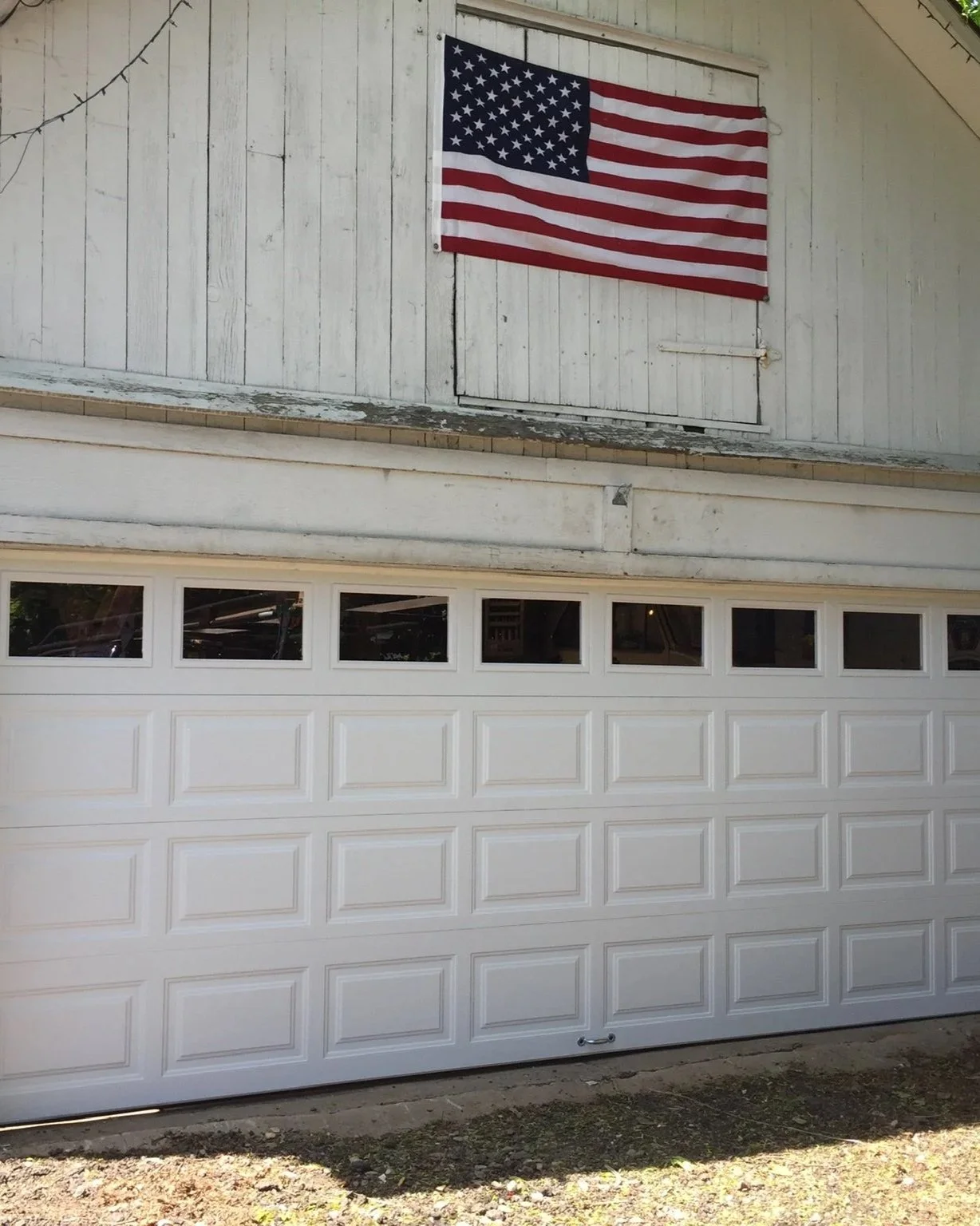American flag hanging on the exterior of a house with a white garage door below.