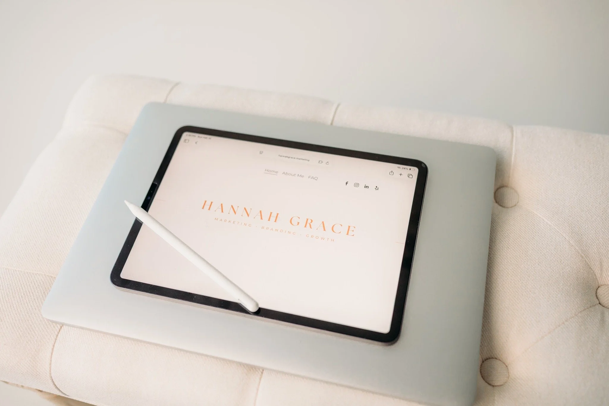A tablet with a stylus on top, displaying a website or branding page for Hannah Grace Marketing, on a white cushion or chair.