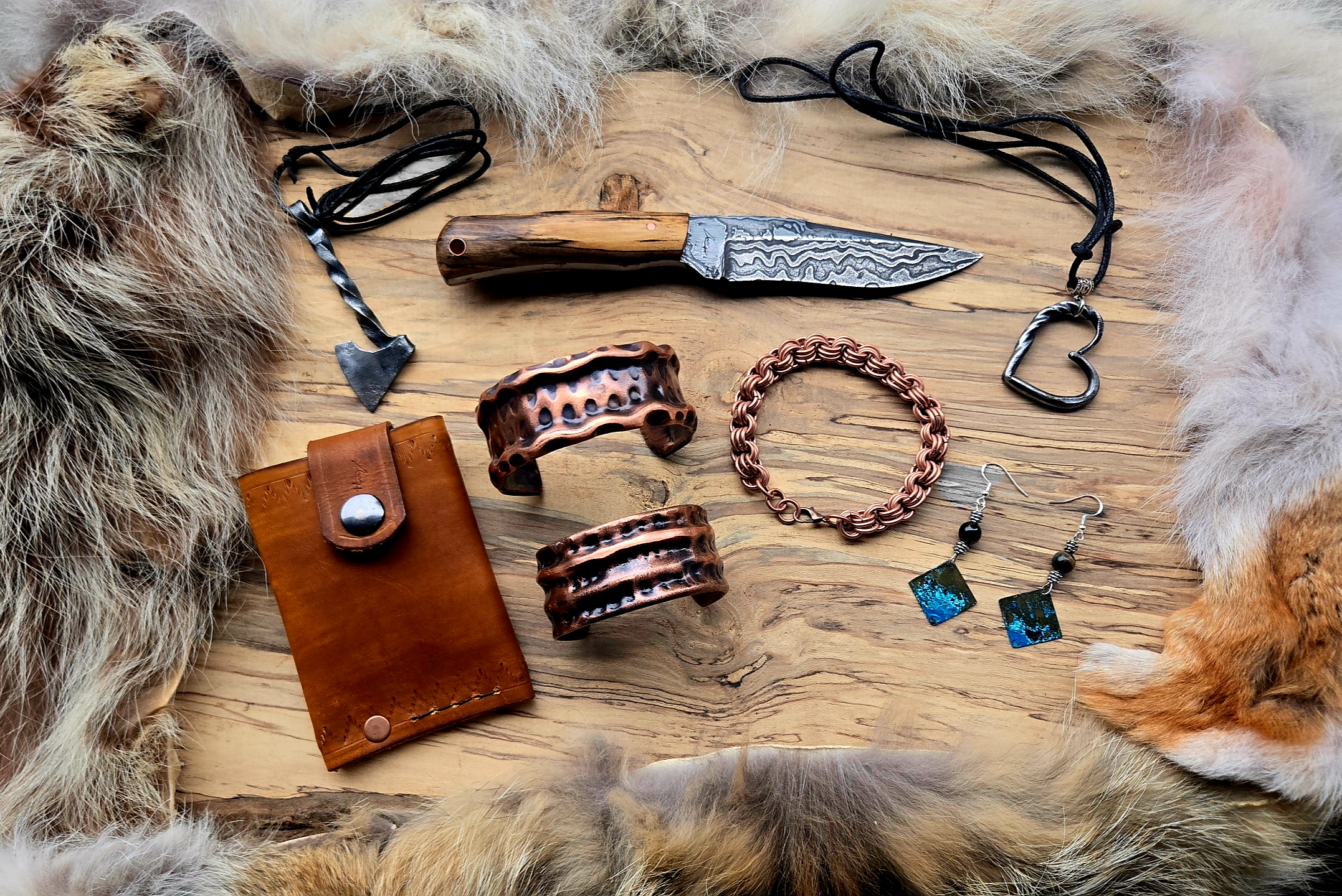 Assorted jewelry and accessories on a wooden surface, framed by animal fur and paws, including a leather wallet, metal bangles, a fishhook necklace, a leather and webbing bracelet, a chain-link bracelet, a pair of dangle earrings, and a Damascus steel knife with a wooden handle.