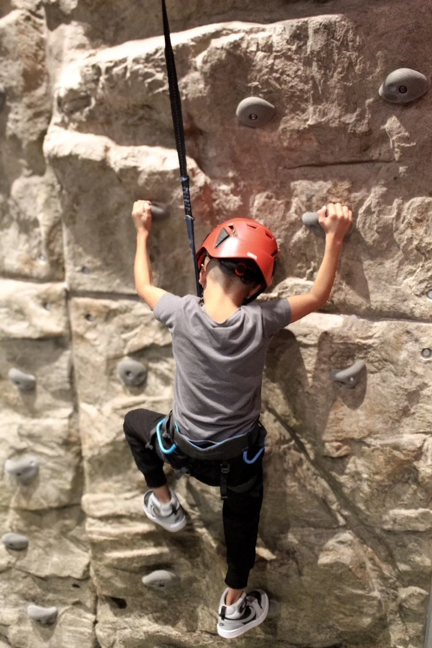 Kid in a red helmet climbing the rock wall at Silver Stone Castle, Swansea, MA