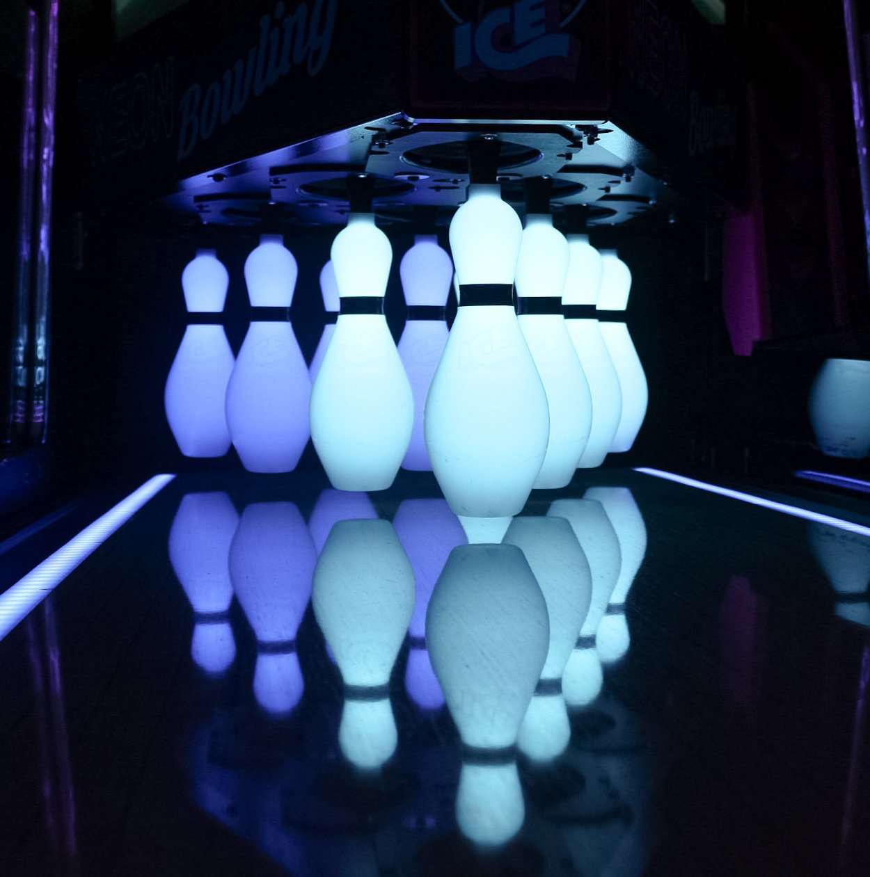 Glowing white bowling pins reflected on a black lane at Neon Bowling, Silver Stone Castle, Swansea, MA