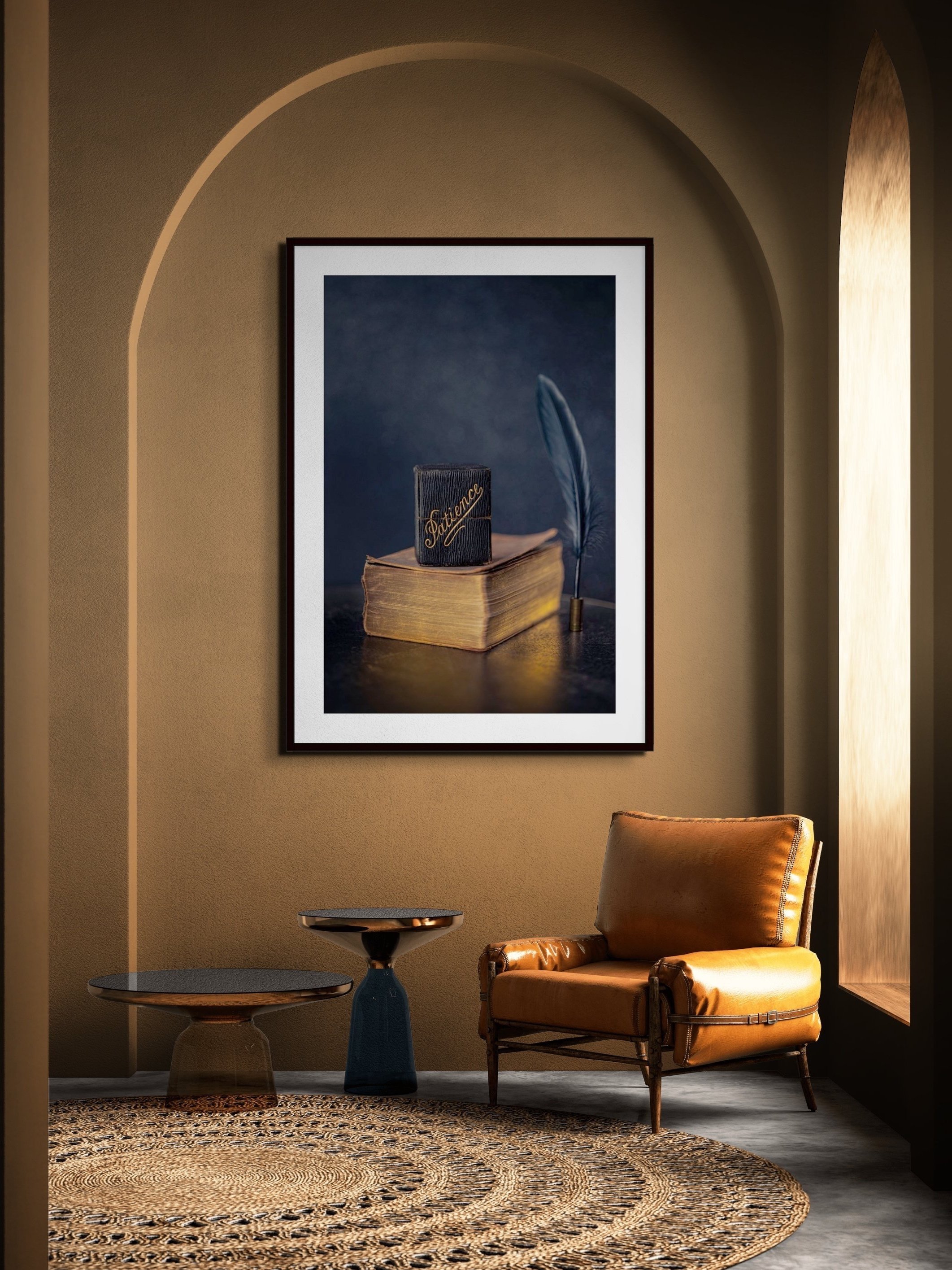 A cozy reading nook with a tan armchair, two small side tables, a framed artwork of a book with a feather, and a textured circular rug.