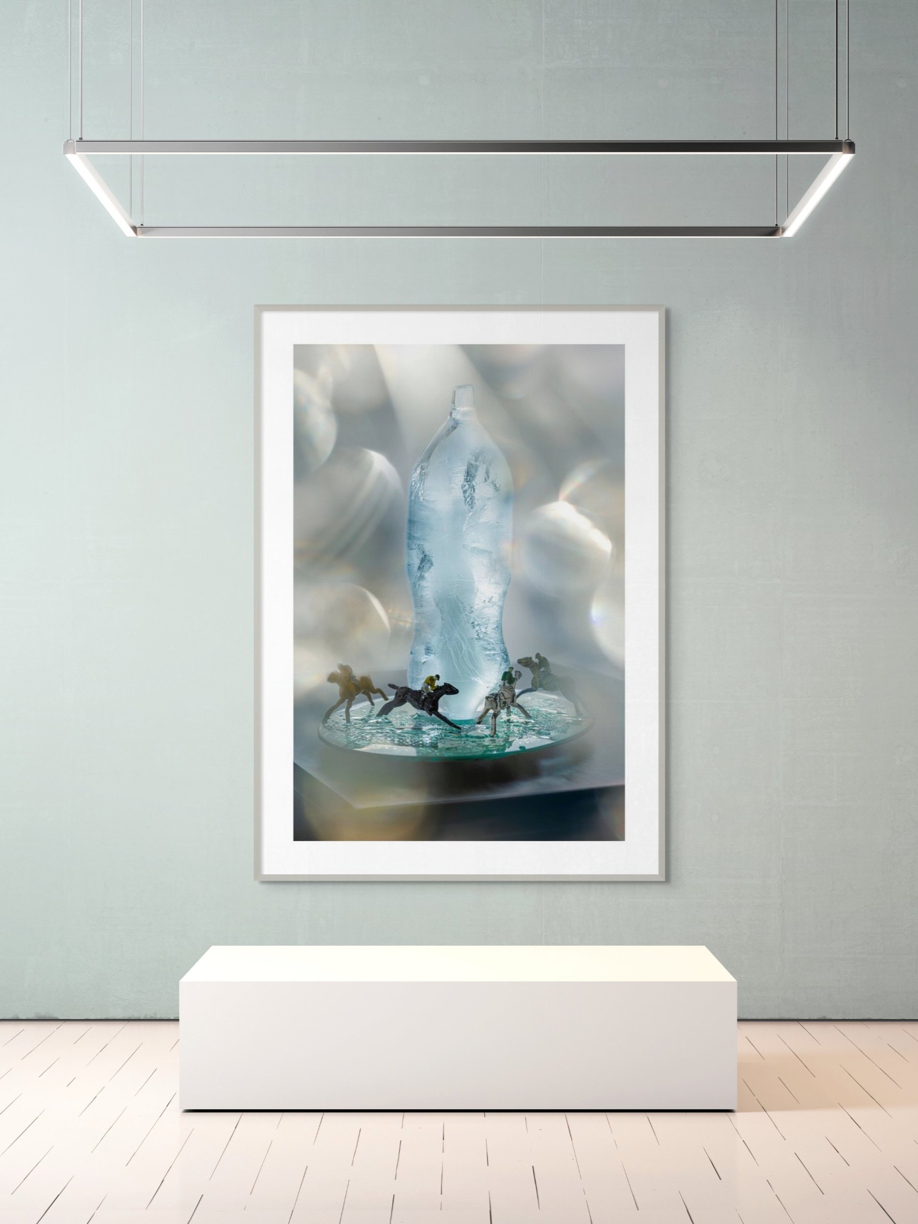 Art print in a gallery showing a close-up of a water bottle with miniatures of snowmobilers in front of it.