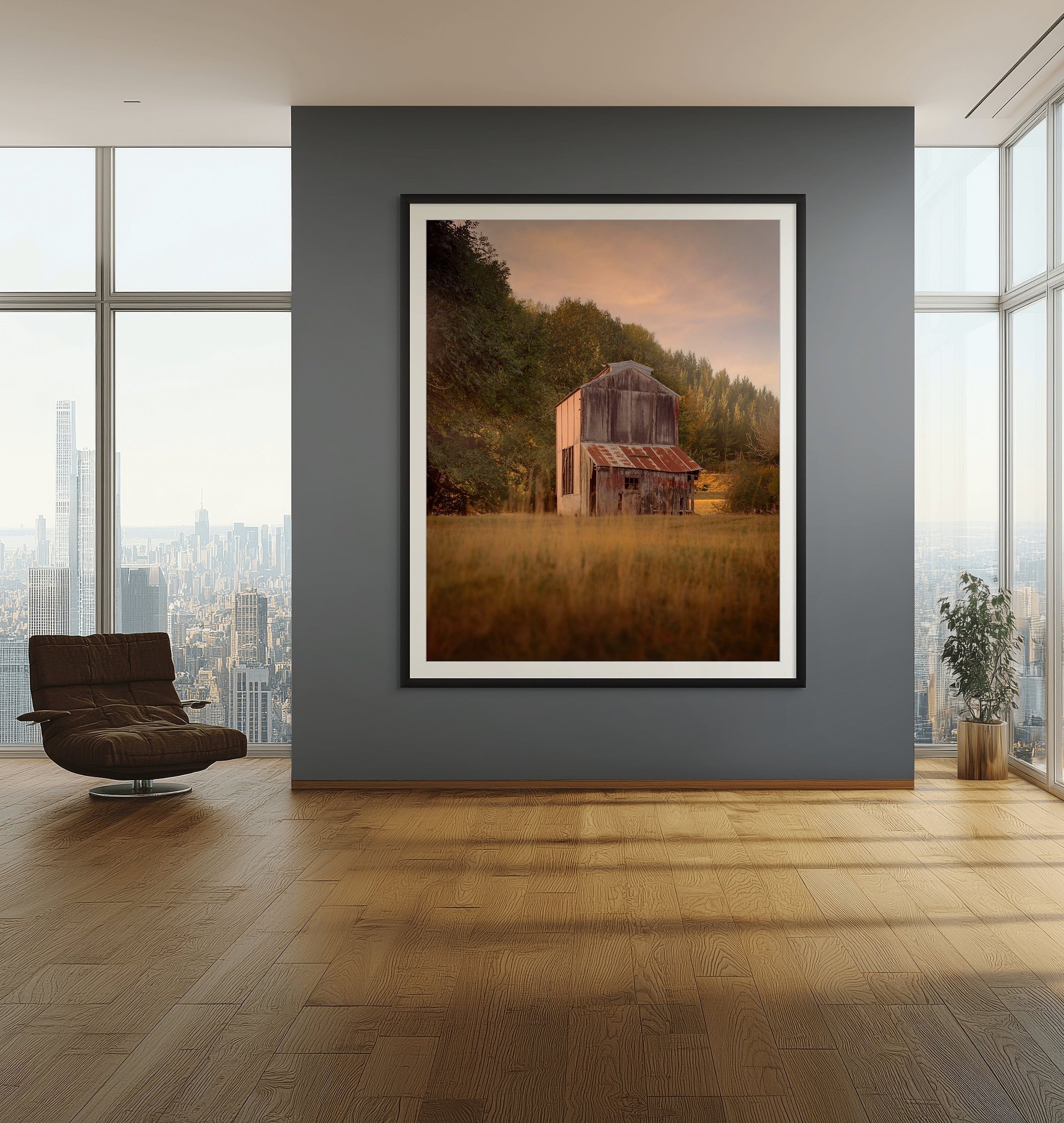 Photograph of an old wooden hop kiln in a grassy field with trees in the background, hung on a dark gray wall in a modern city apartment with floor-to-ceiling windows and city skyline view.