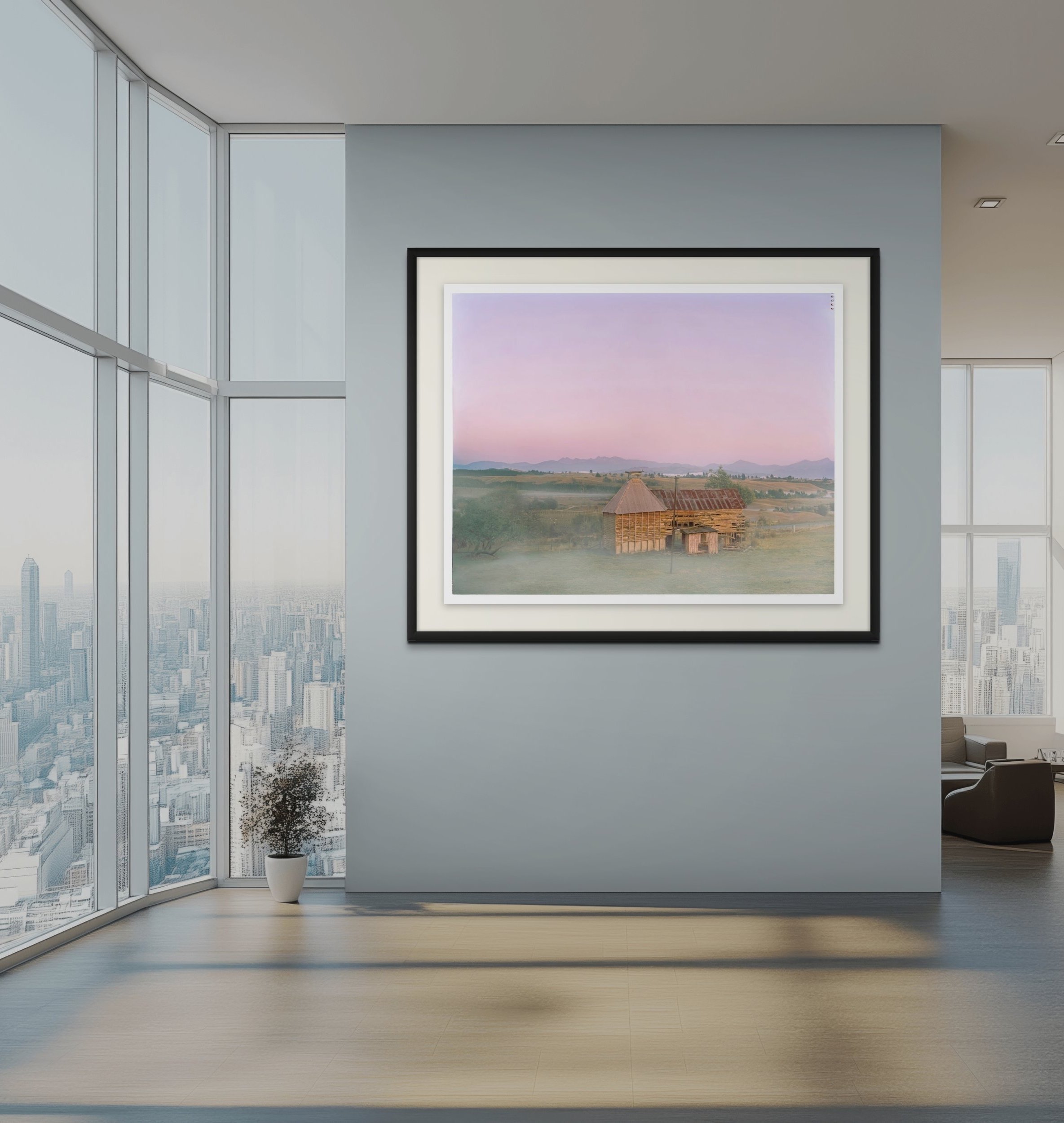Modern high-rise office with large windows and city skyline view, featuring a framed landscape painting of a pastoral  showing an old wooden hop kiln scene hanging on a gray wall.