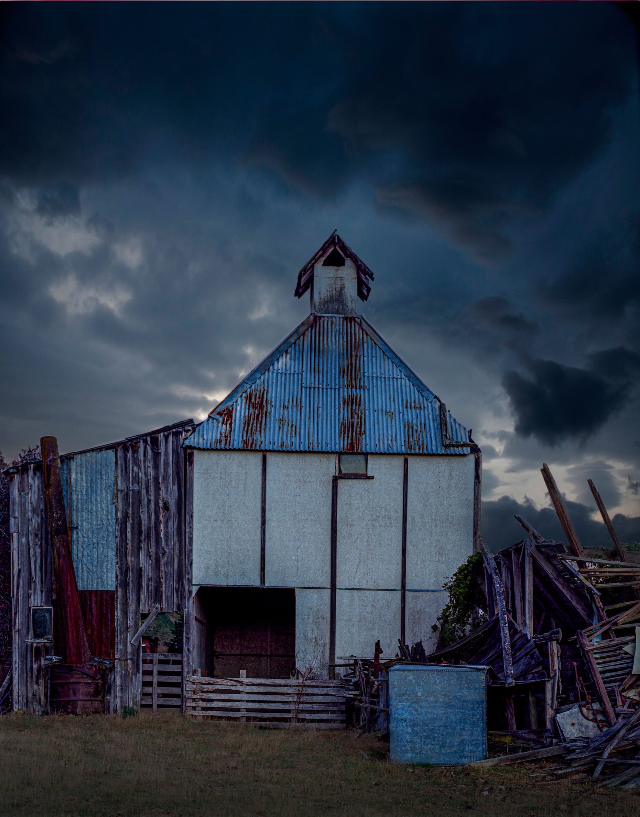 Old abandoned hop kiln with rusty tin roof under dark stormy sky.
