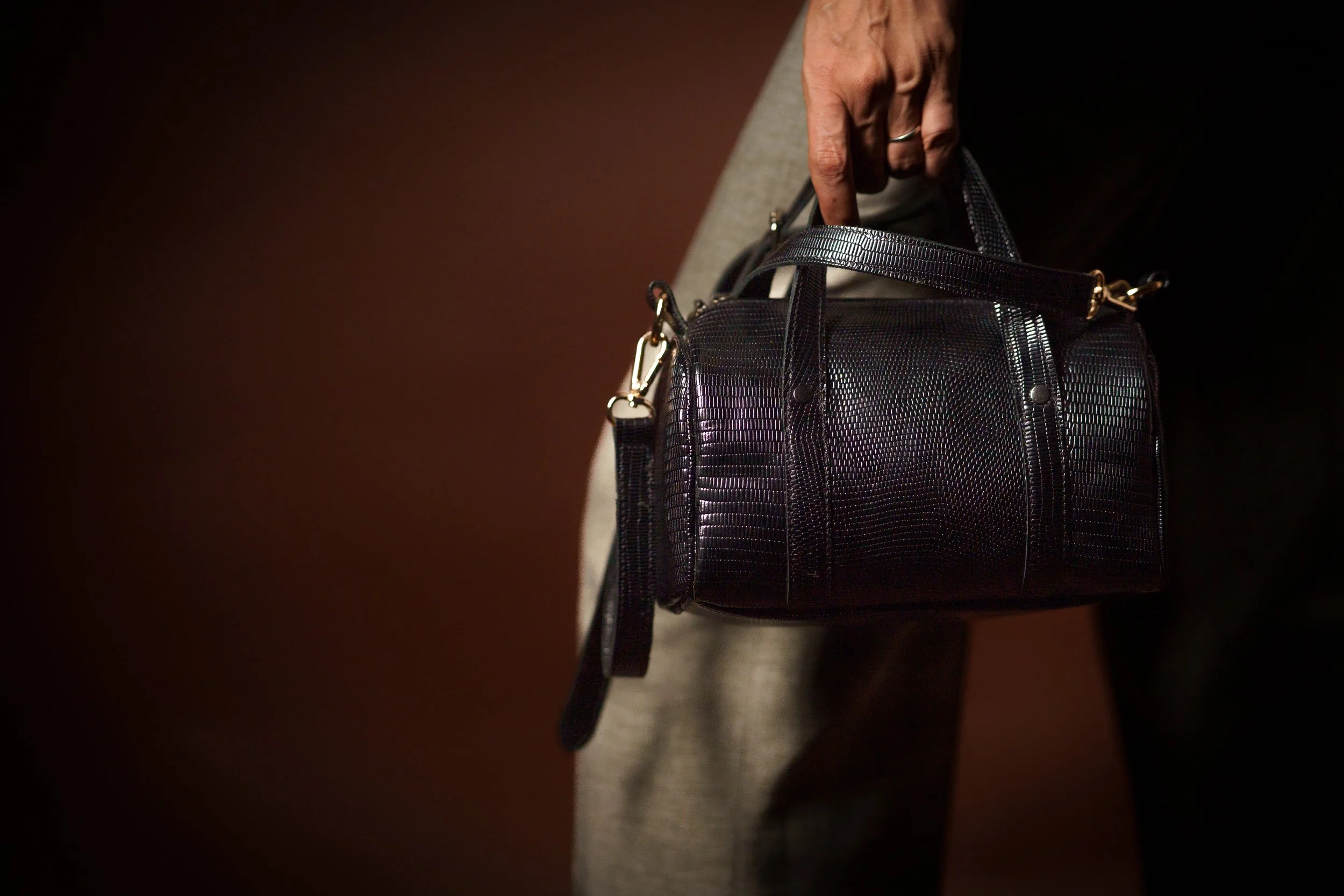 Person holding a small black handbag with textured surface against a dark background.