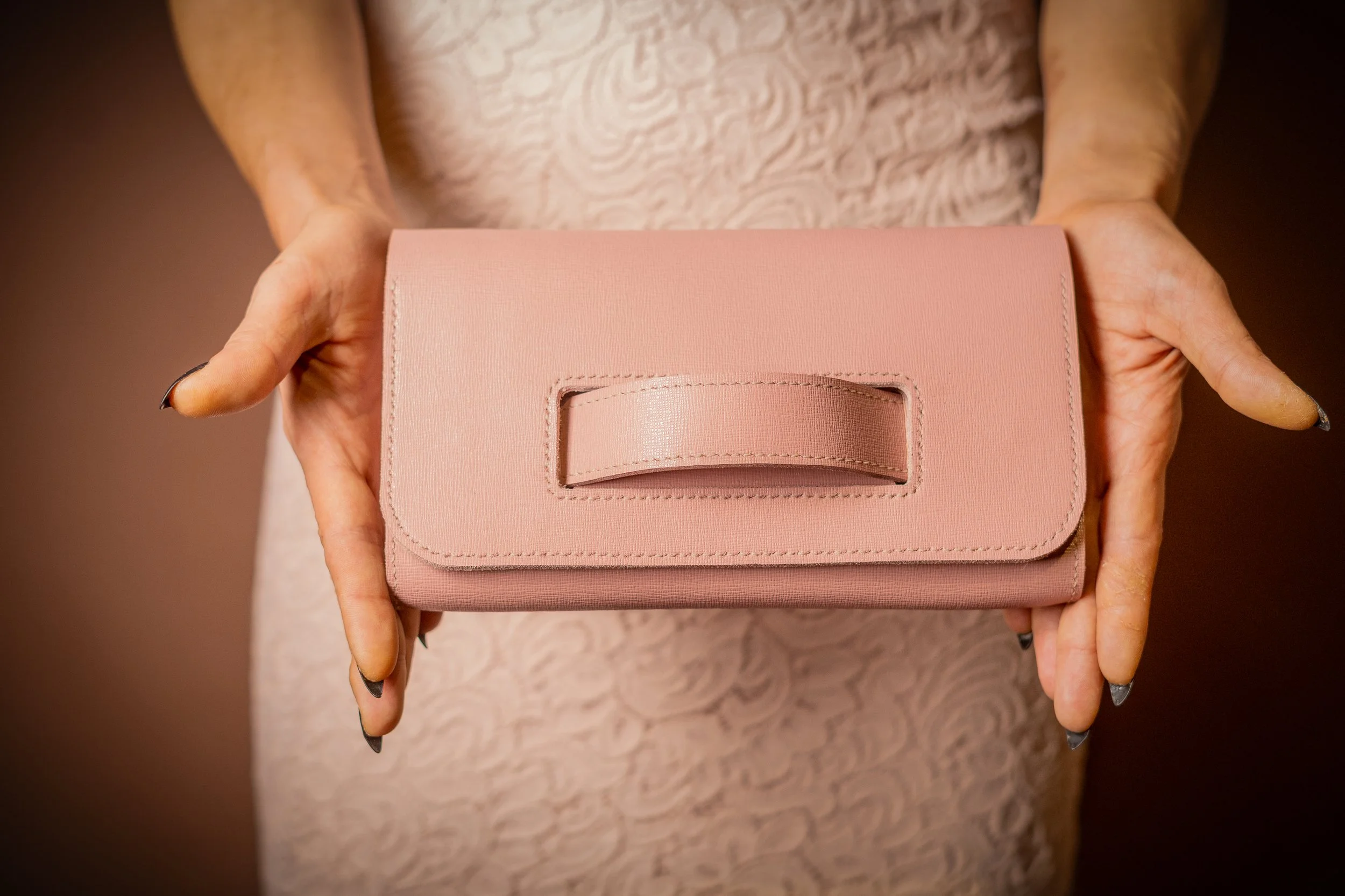 Person holding a pink clutch purse with a handle on the front