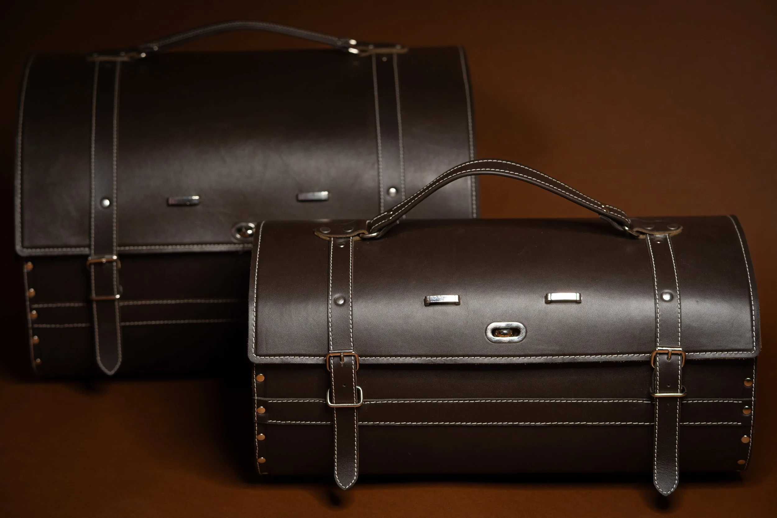Two vintage leather doctor bags with metal buckles and stitching on a wooden surface.