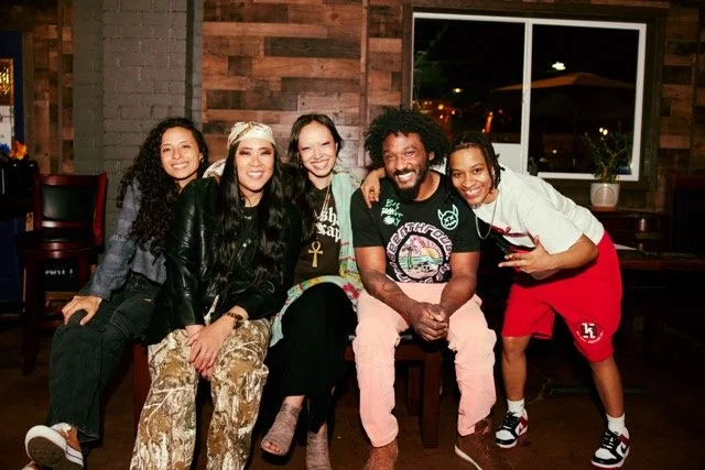 Five friends sitting together in a cozy restaurant, smiling for the camera.