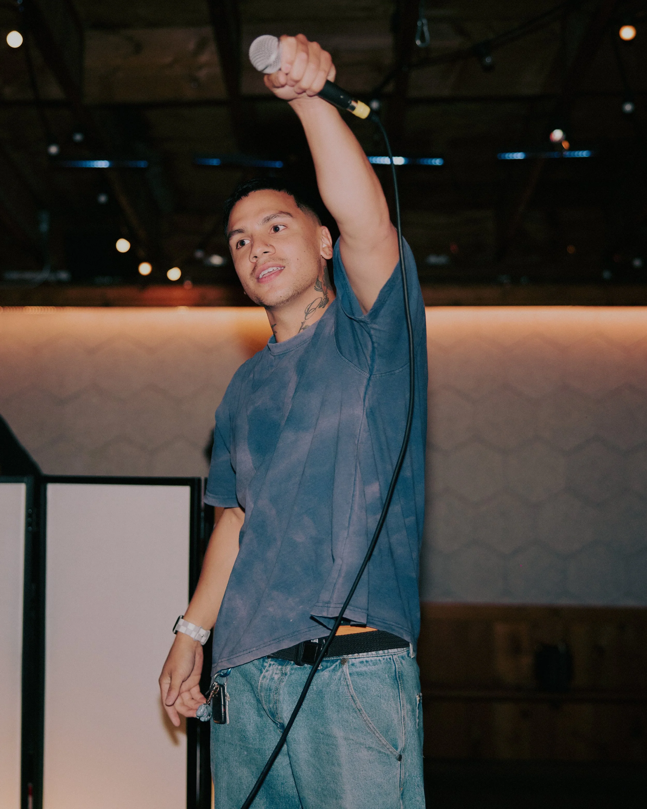 A young man holding a microphone in the air, likely on stage or in a performance setting.