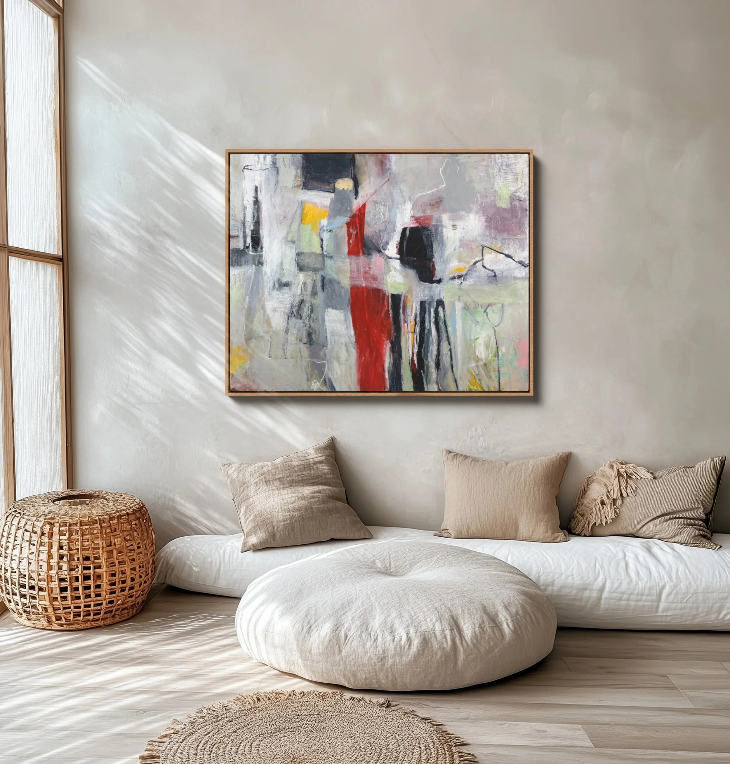 A bedroom with a blank cream-colored wall, a framed abstract painting with bold colors and brushstrokes, beige pillows on a bed with a white cover, a woven rattan basket, and a textured round rug on light wooden floor.