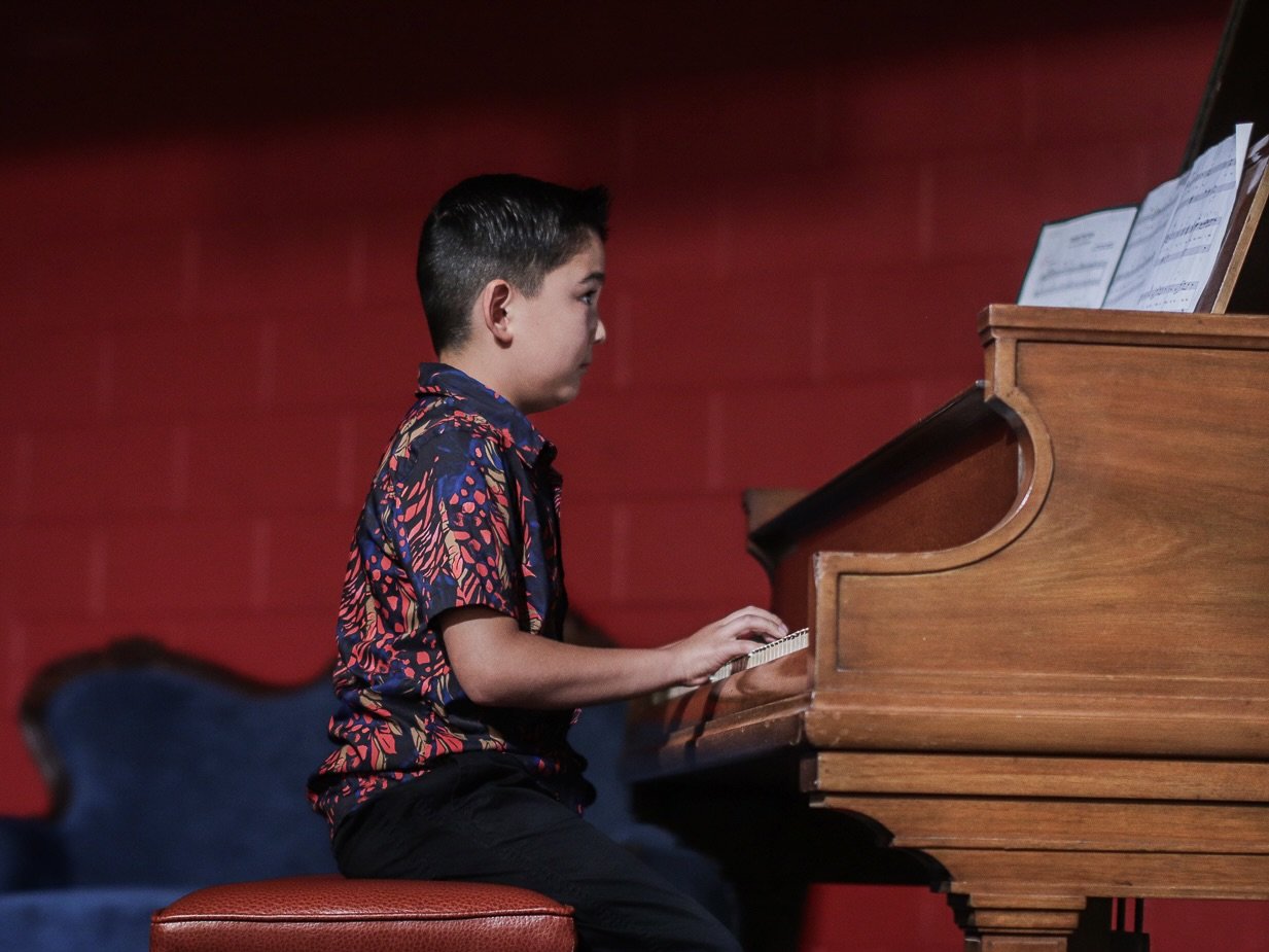 A boy playing a piano in a room with red walls.