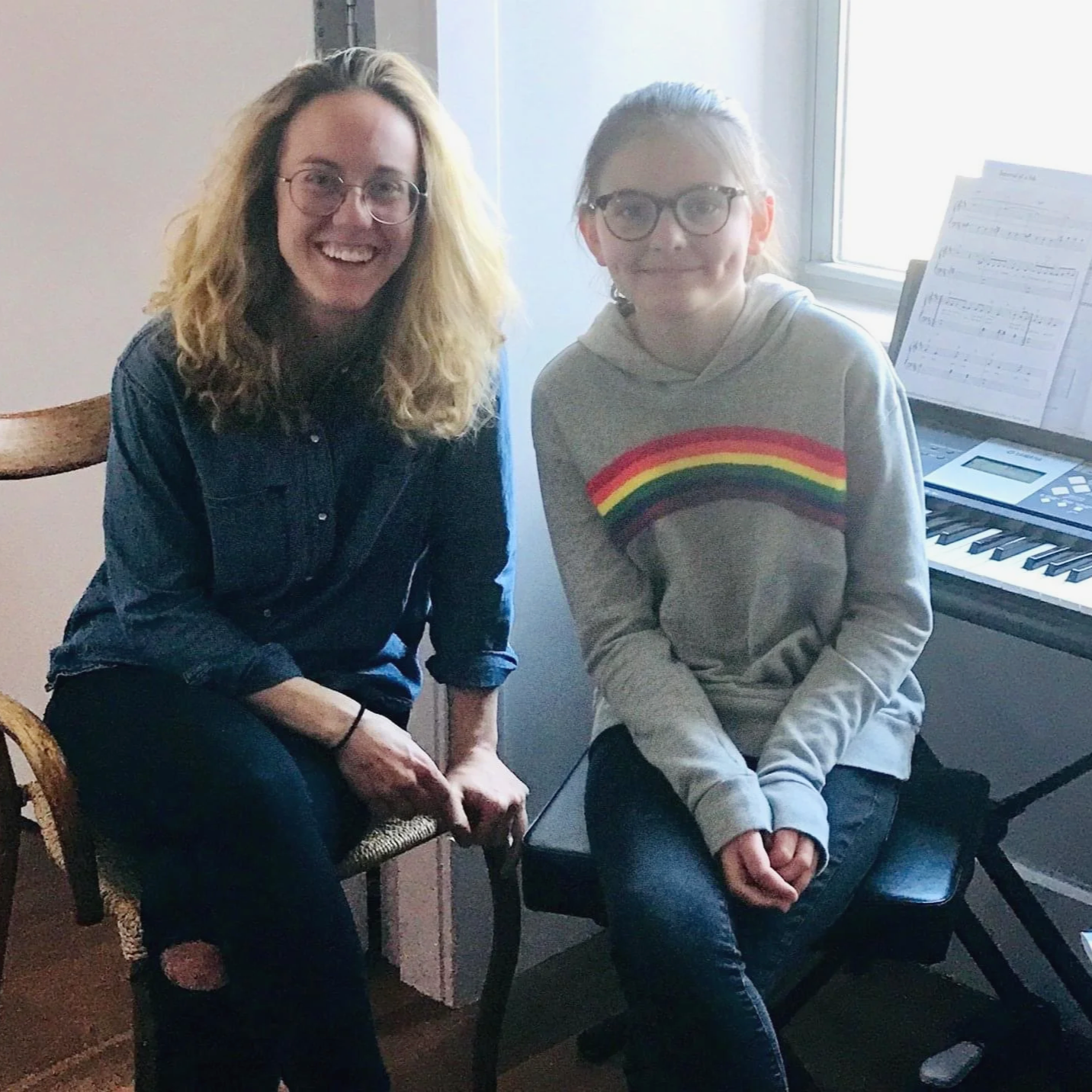piano teacher and young girl sit at keyboard