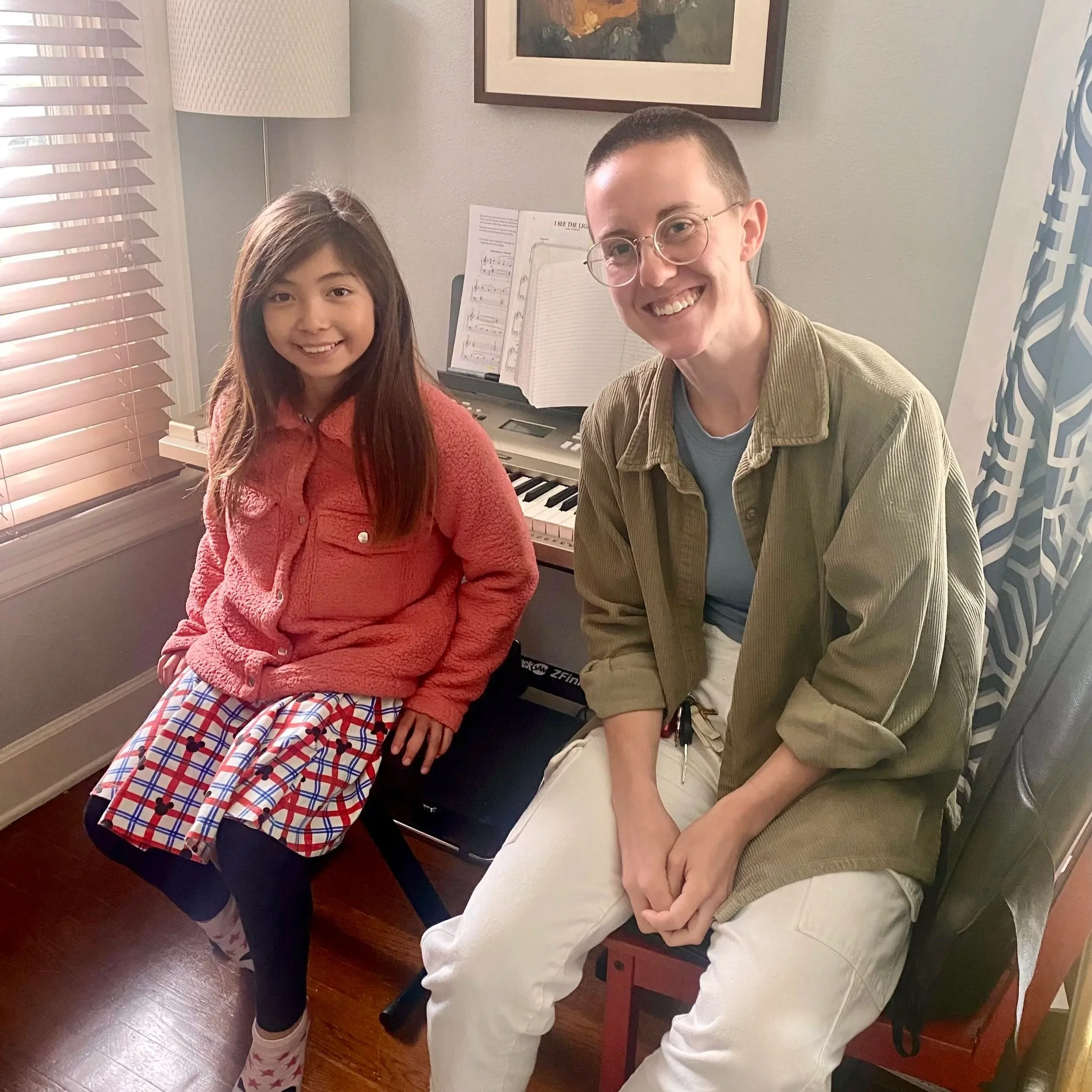 A young girl and an adult woman sitting indoors next to a keyboard, both smiling at the camera.