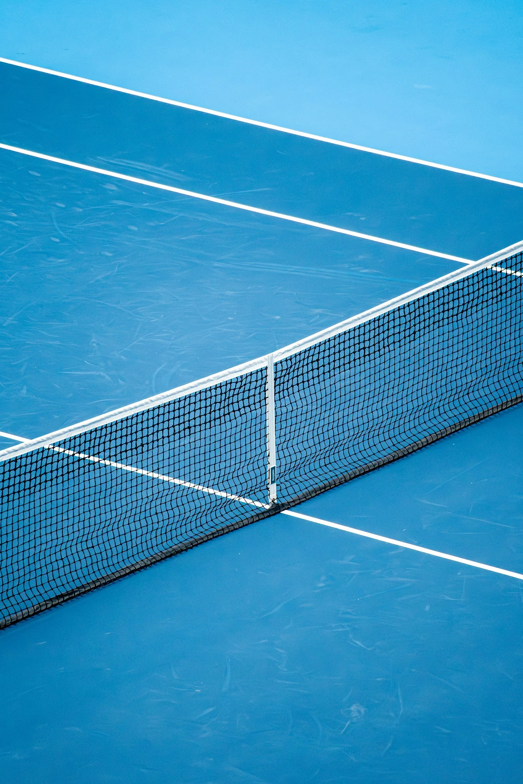 Empty blue tennis court with a black net dividing the court in the middle.