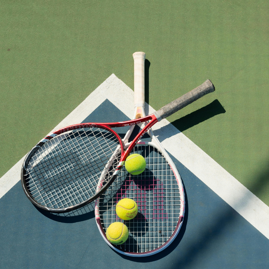 Two tennis rackets and three tennis balls on a tennis court.