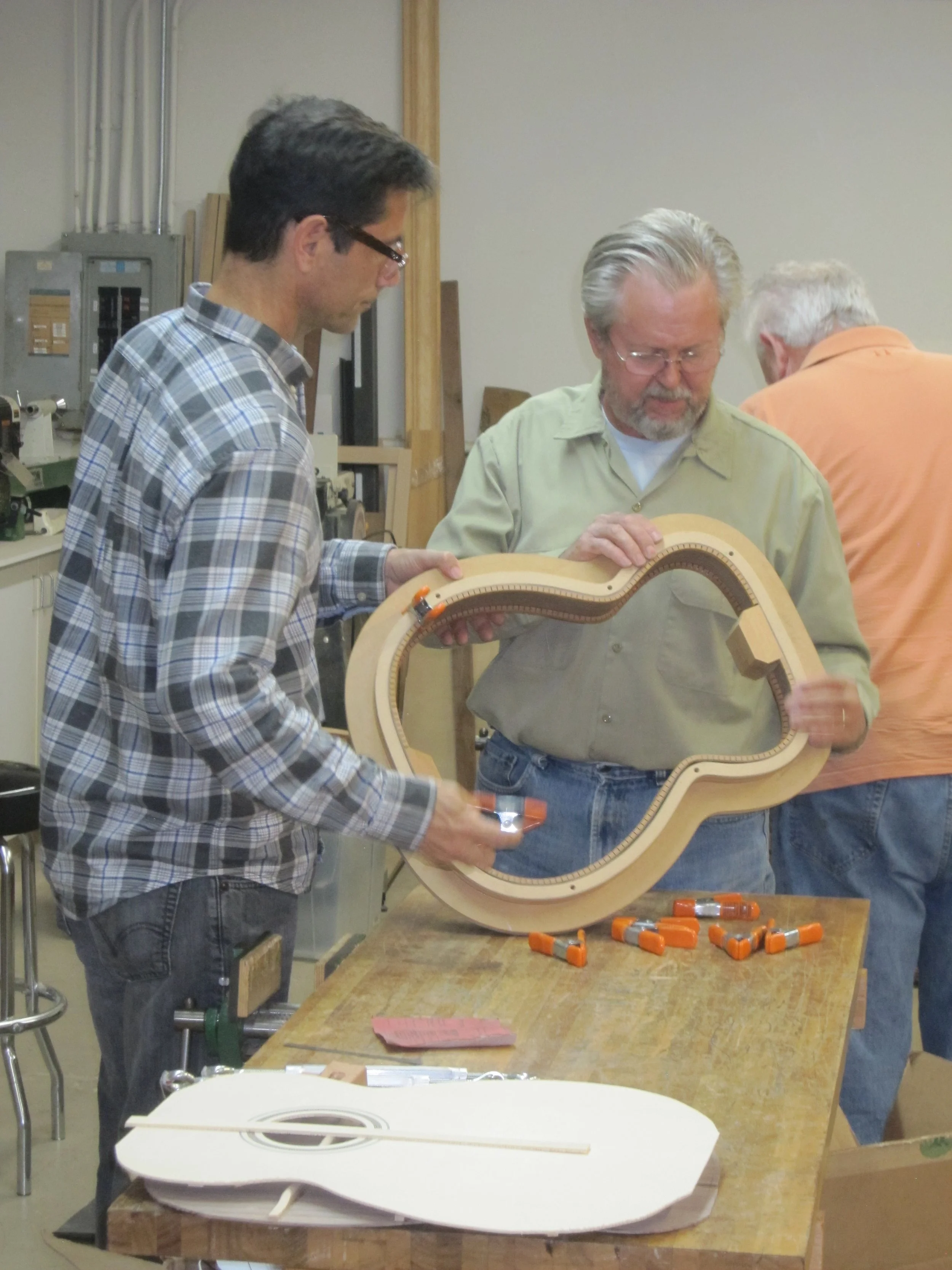 Guitarmaking instructor Eric Nichols inspects a student's guitar body, which is clamped into a guitar mold.