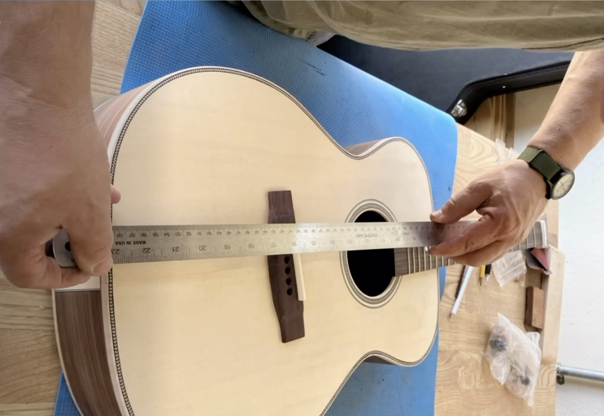 Photo of hands holding a steel ruler to measure the height of a bridge saddle on an acoustic guitar.