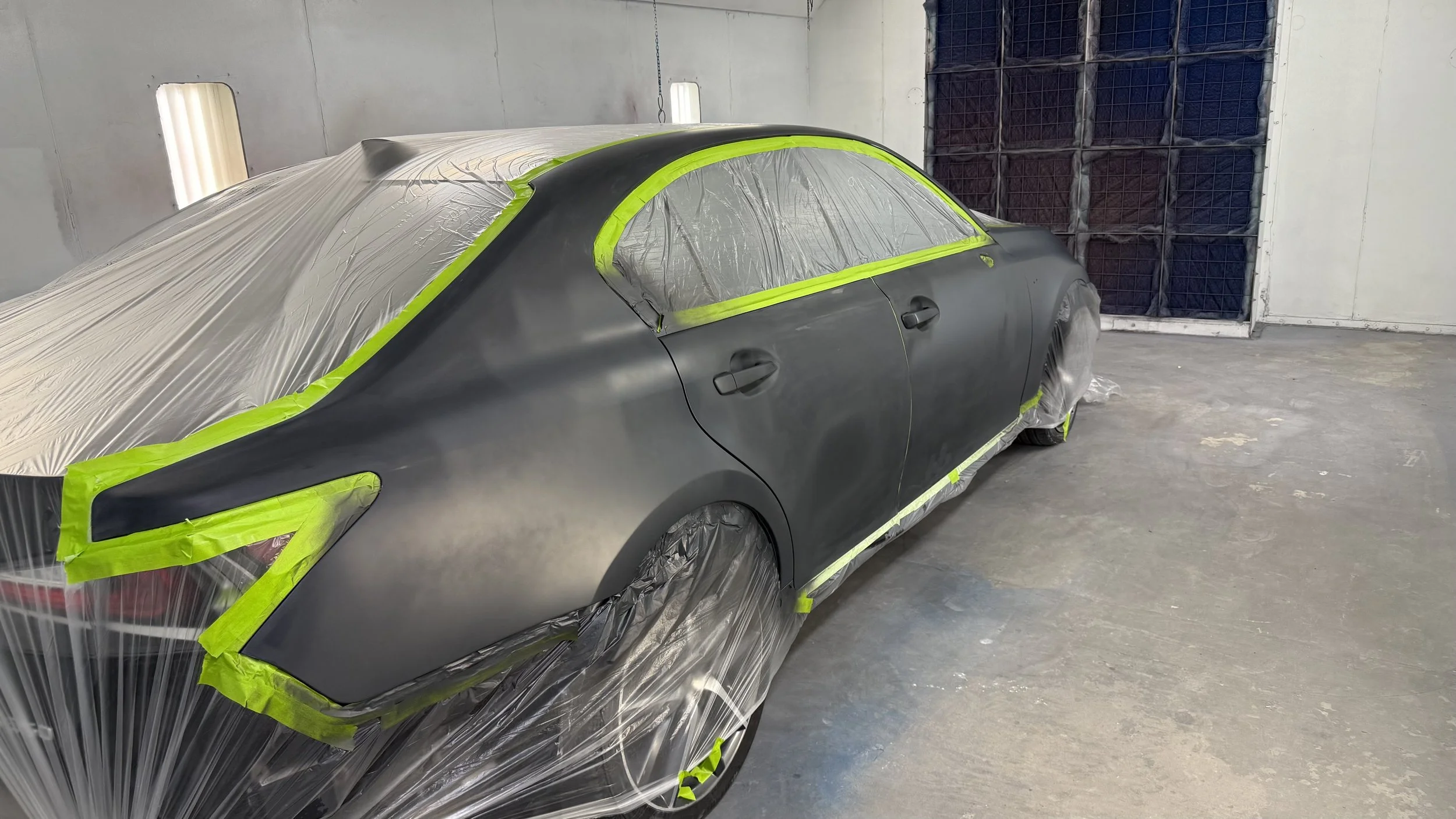 A car in a painting booth covered with protective plastic and tape, preparing for painting.