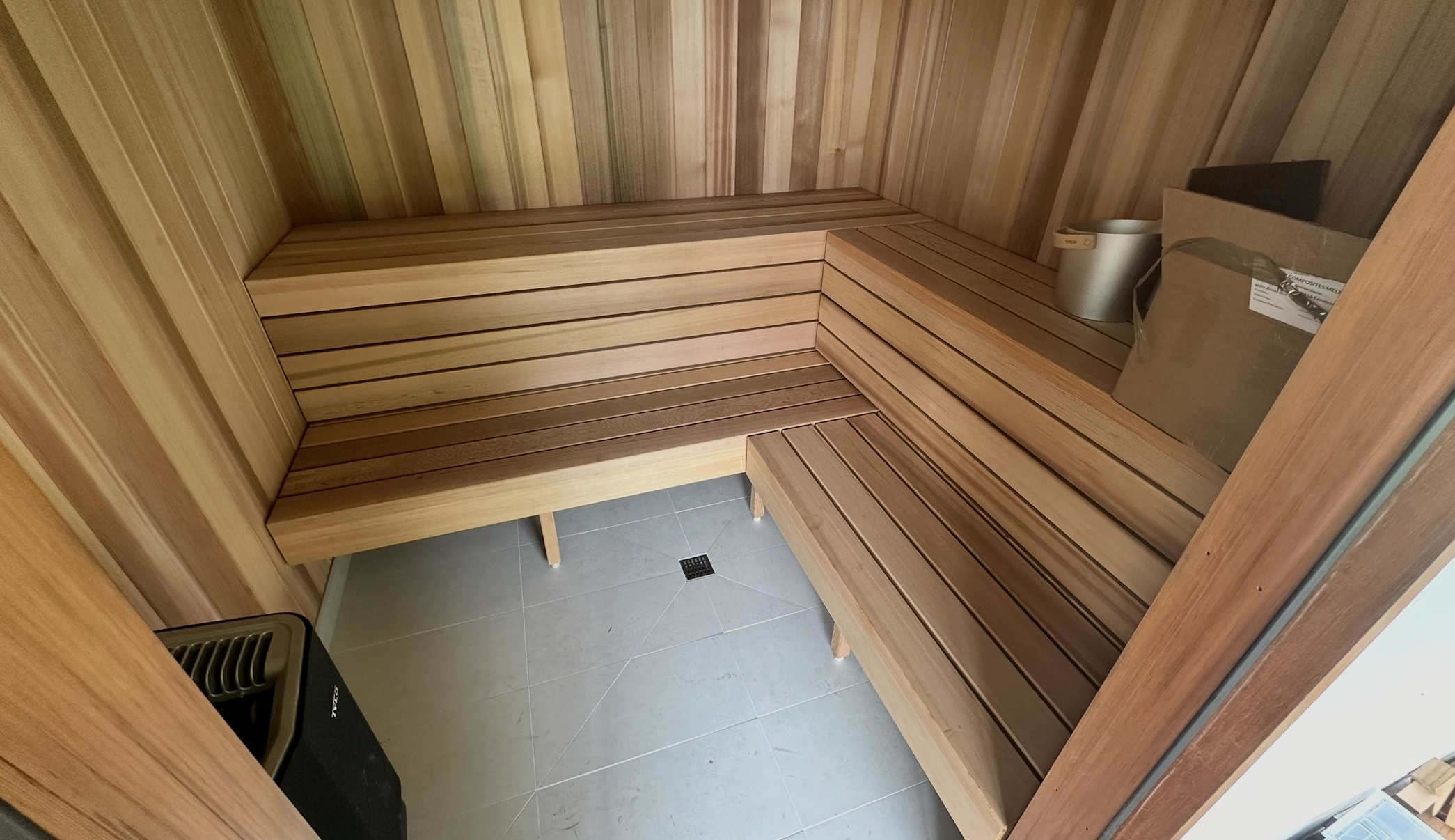 Wooden sauna room with benches and a small heater in the corner.