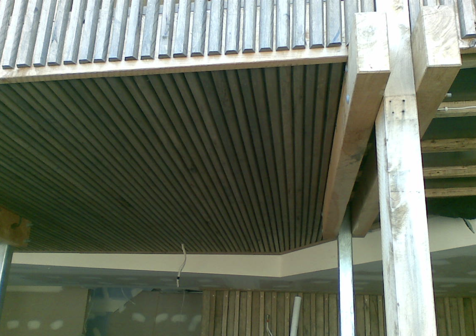 Close-up view of a ceiling with wooden slats, part of a building under construction with visible support beams and unfinished interior.