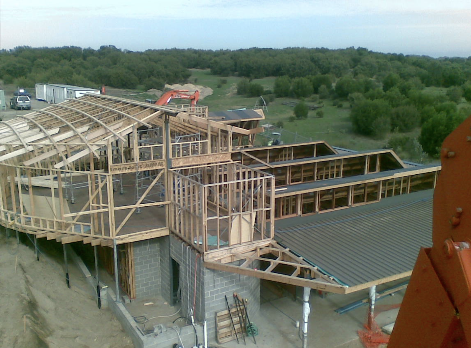 Construction site of a house with wooden framing and concrete block foundation, surrounded by green landscape.