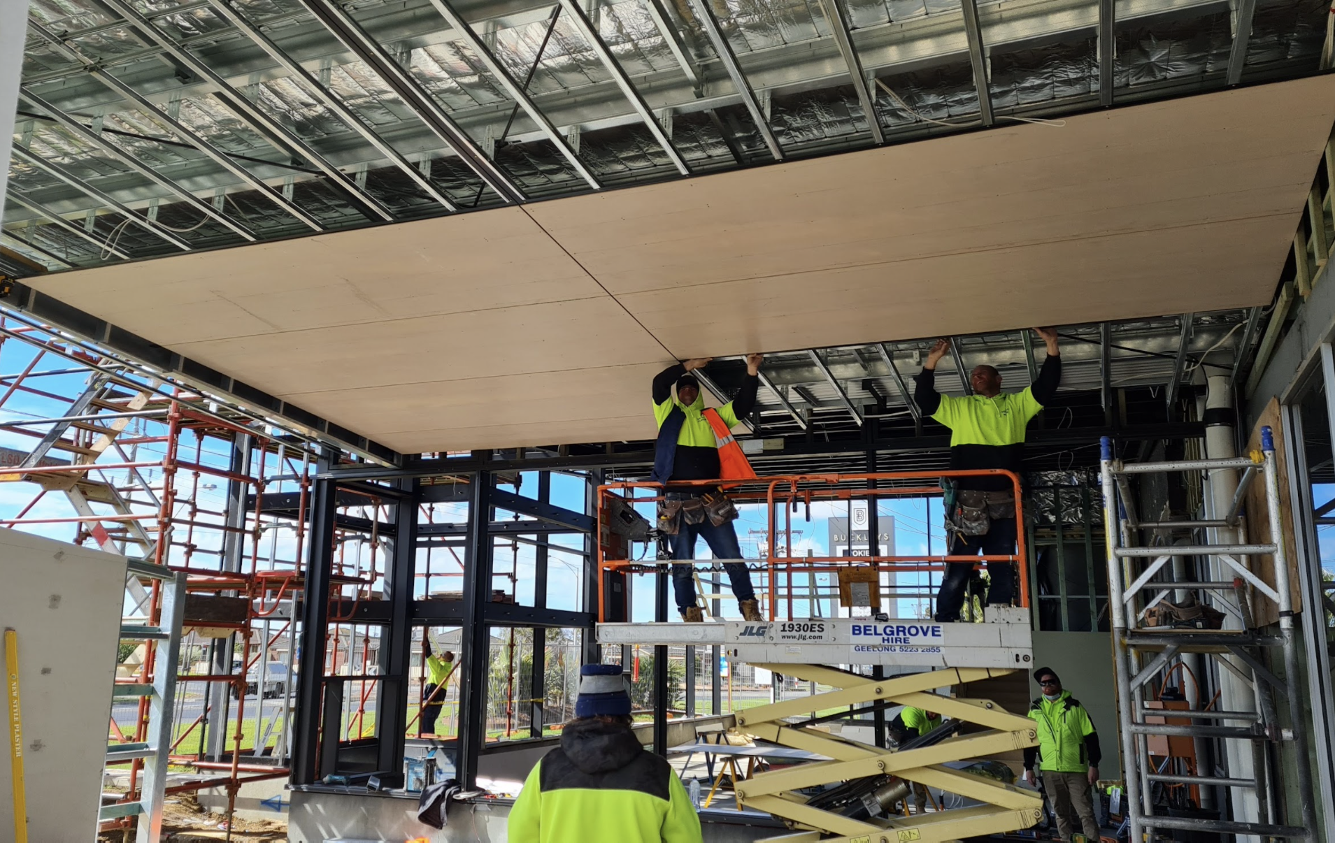 Construction workers installing a large ceiling panel inside a building under construction.