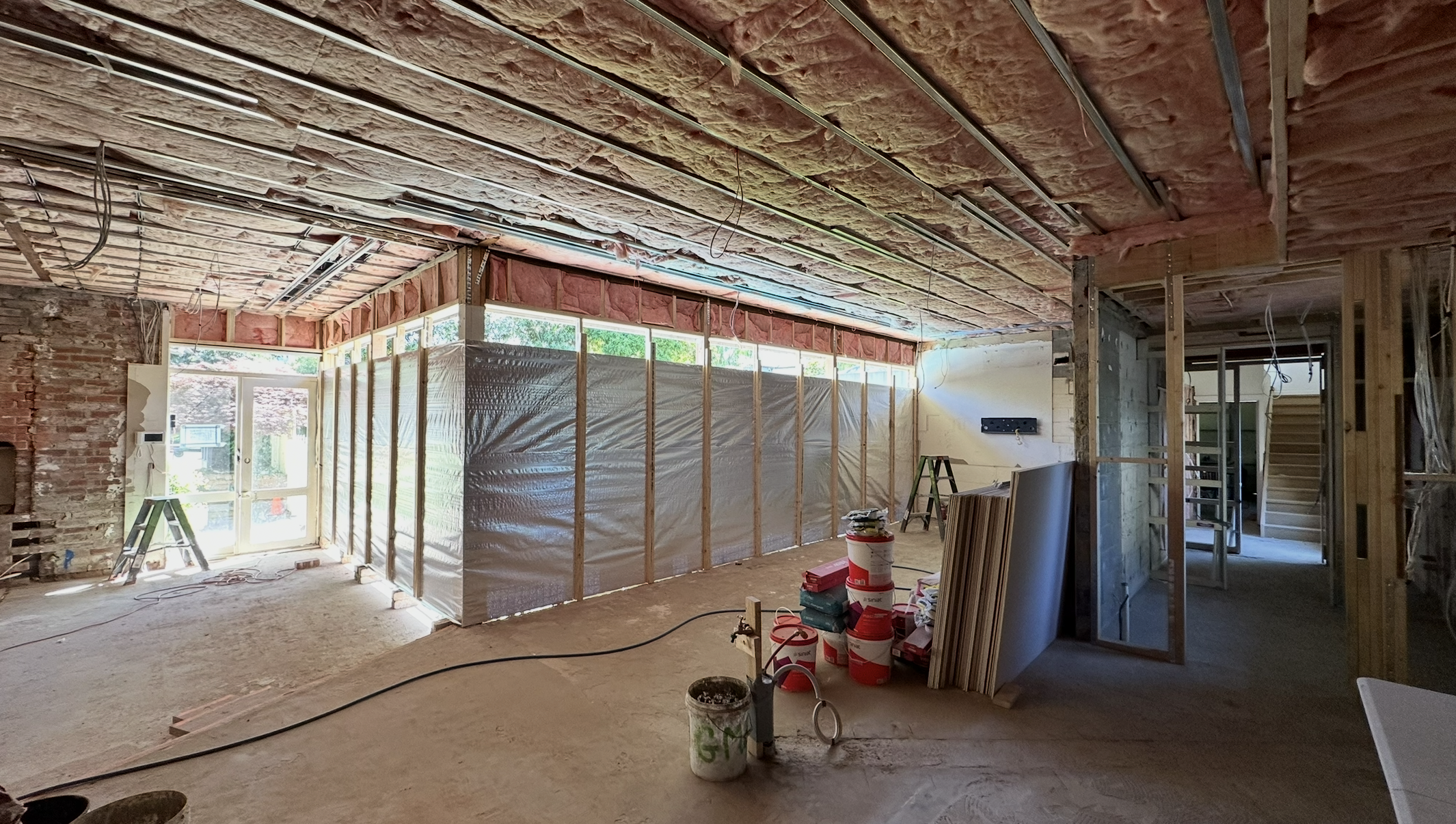 Interior of a house under construction with exposed insulation and framing, construction tools, and building materials.