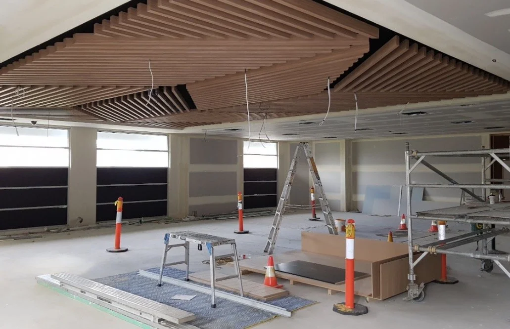 Construction site of a warehouse with black metal walls and framing, concrete flooring, and construction equipment outdoors