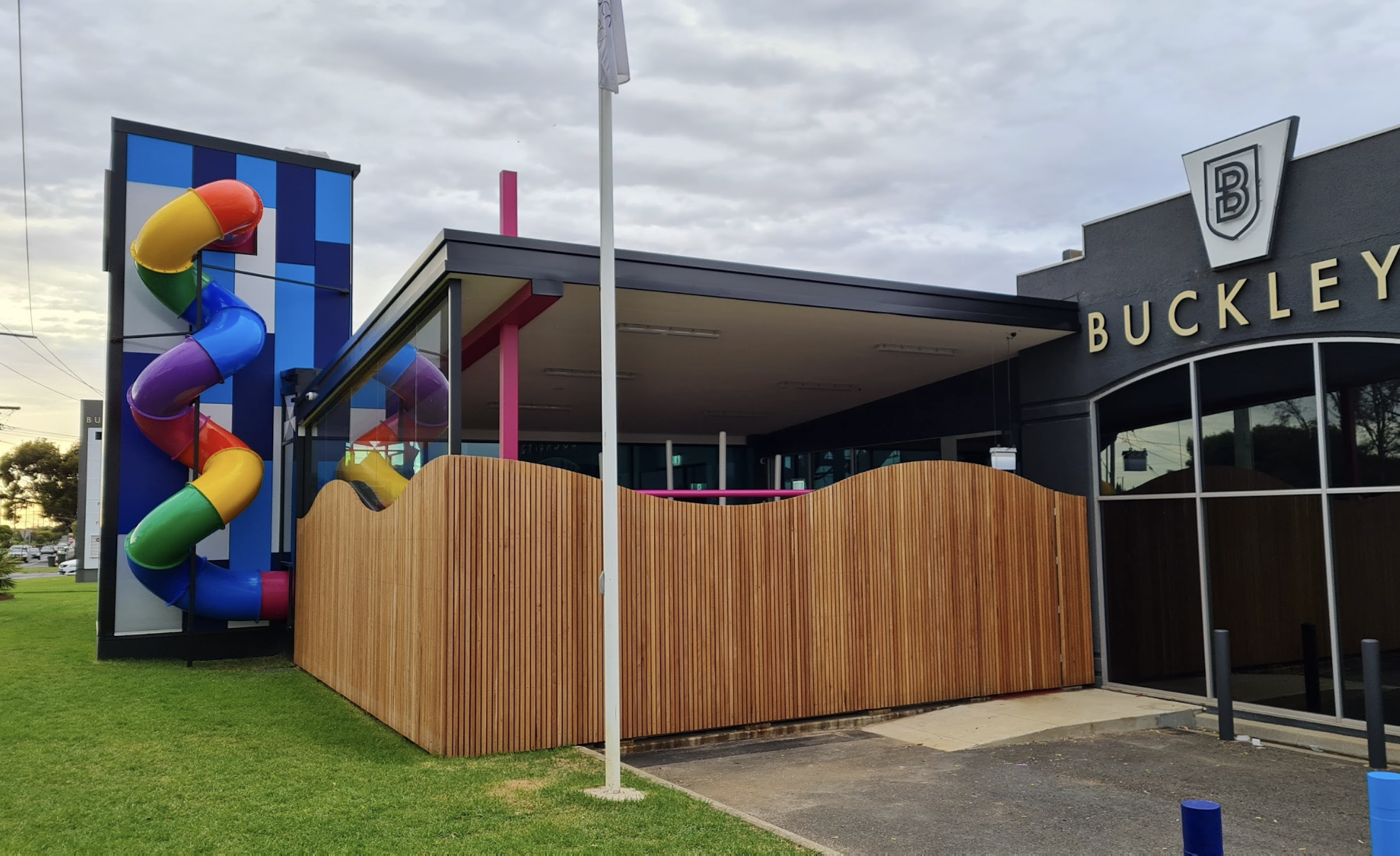 Exterior of a restaurant or cafe named Buckley's with a colorful outdoor slide and a wooden fence. The sky is overcast.